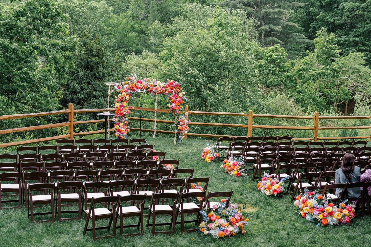 Outdoor wedding ceremony setup with brown chairs and a floral arch against a scenic mountain backdrop.