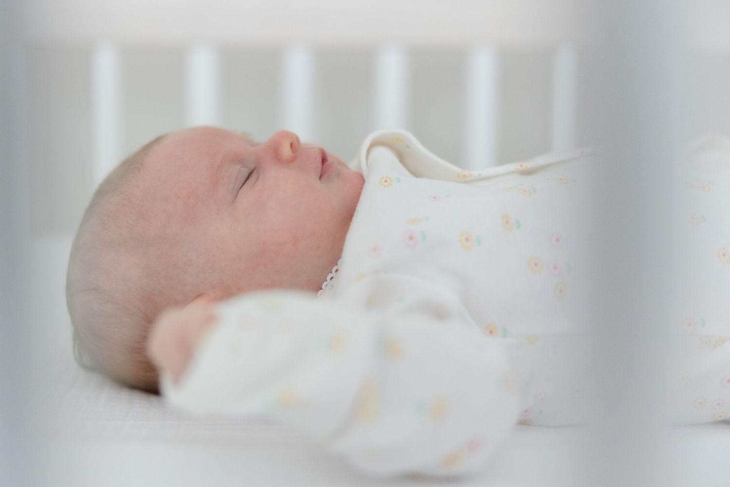 A peaceful sleeping baby wearing a white polka dot sleeper lies in a crib.
