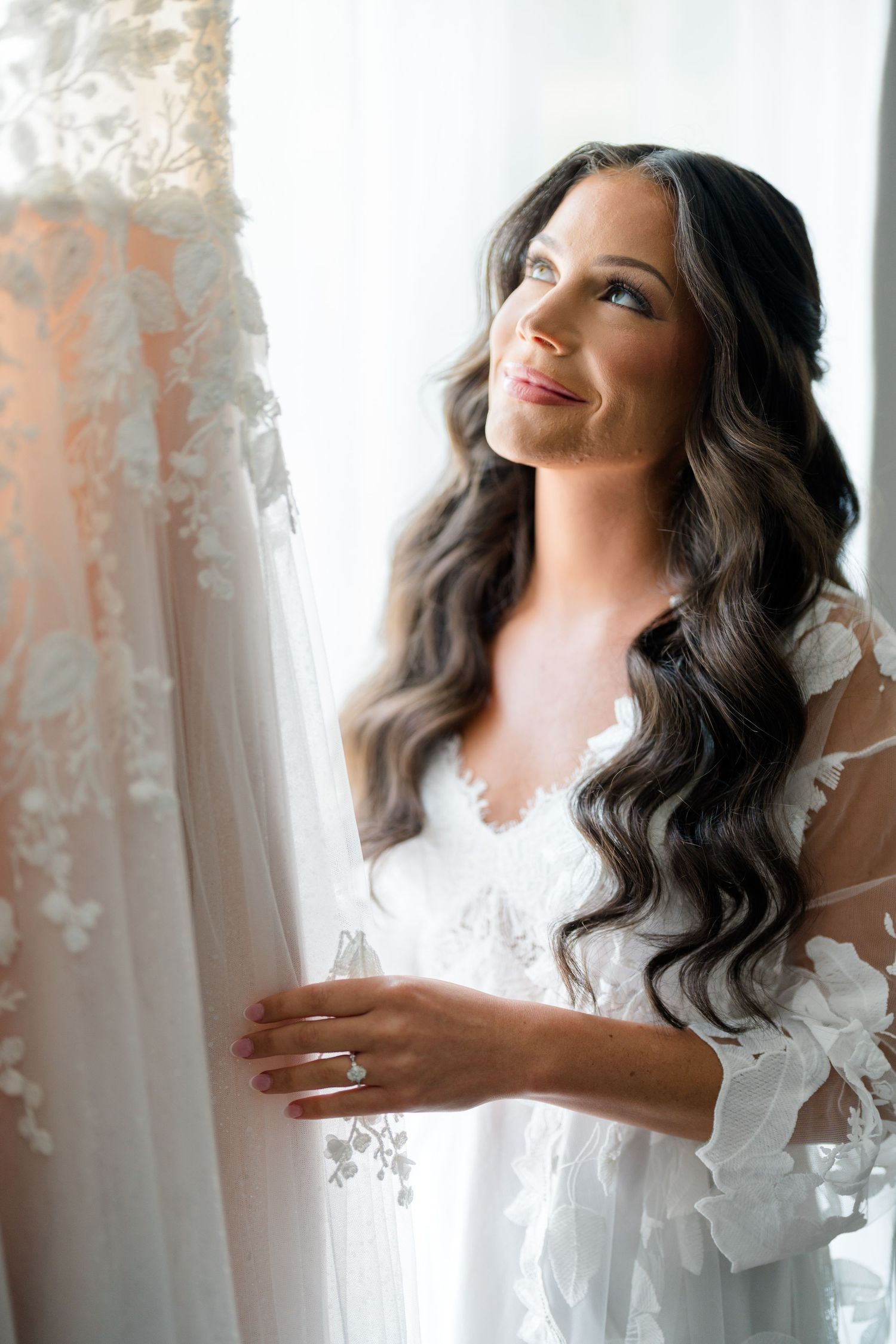 Artistic bridal portrait with flowing lace dress against white curtains.