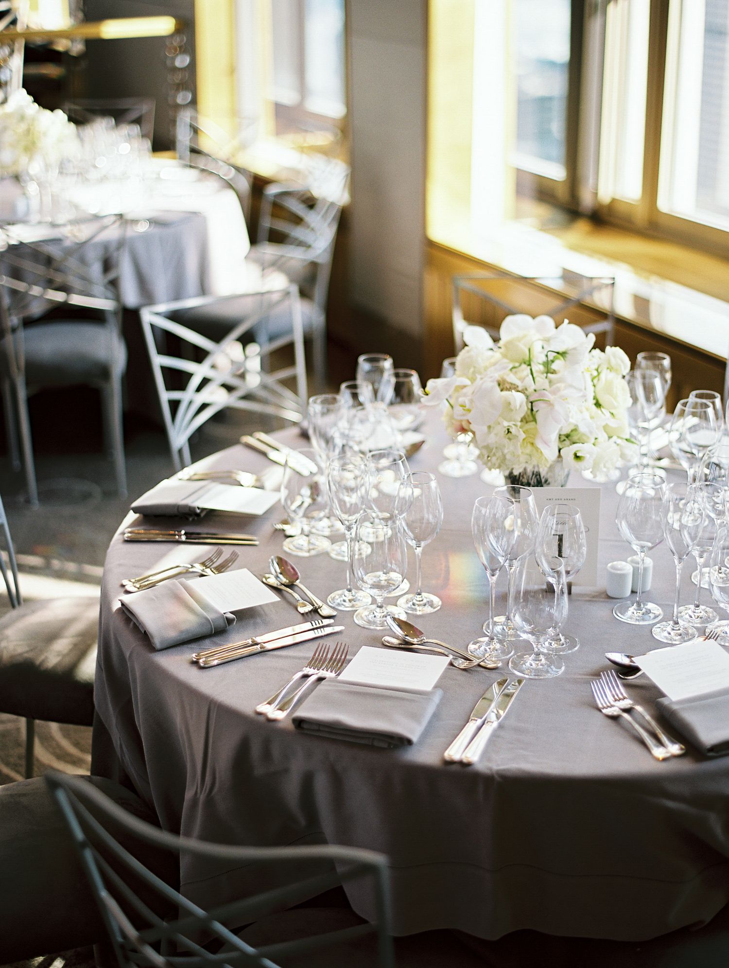 Round dining tables decorated with white floral arrangements and formal place settings for an elegant event.