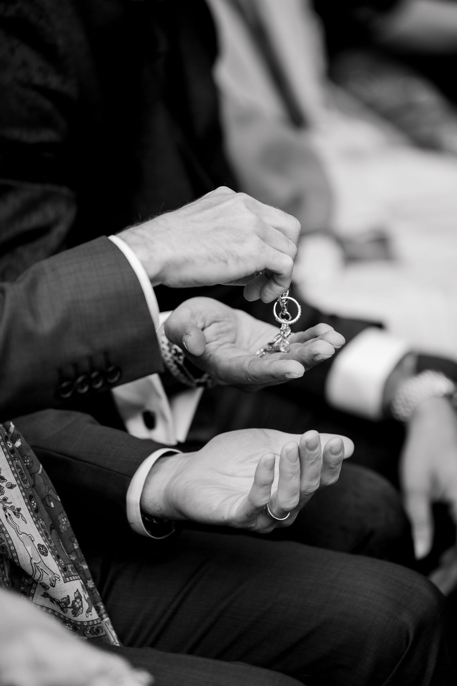 Black and white close-up of hands holding wedding rings during ceremony.