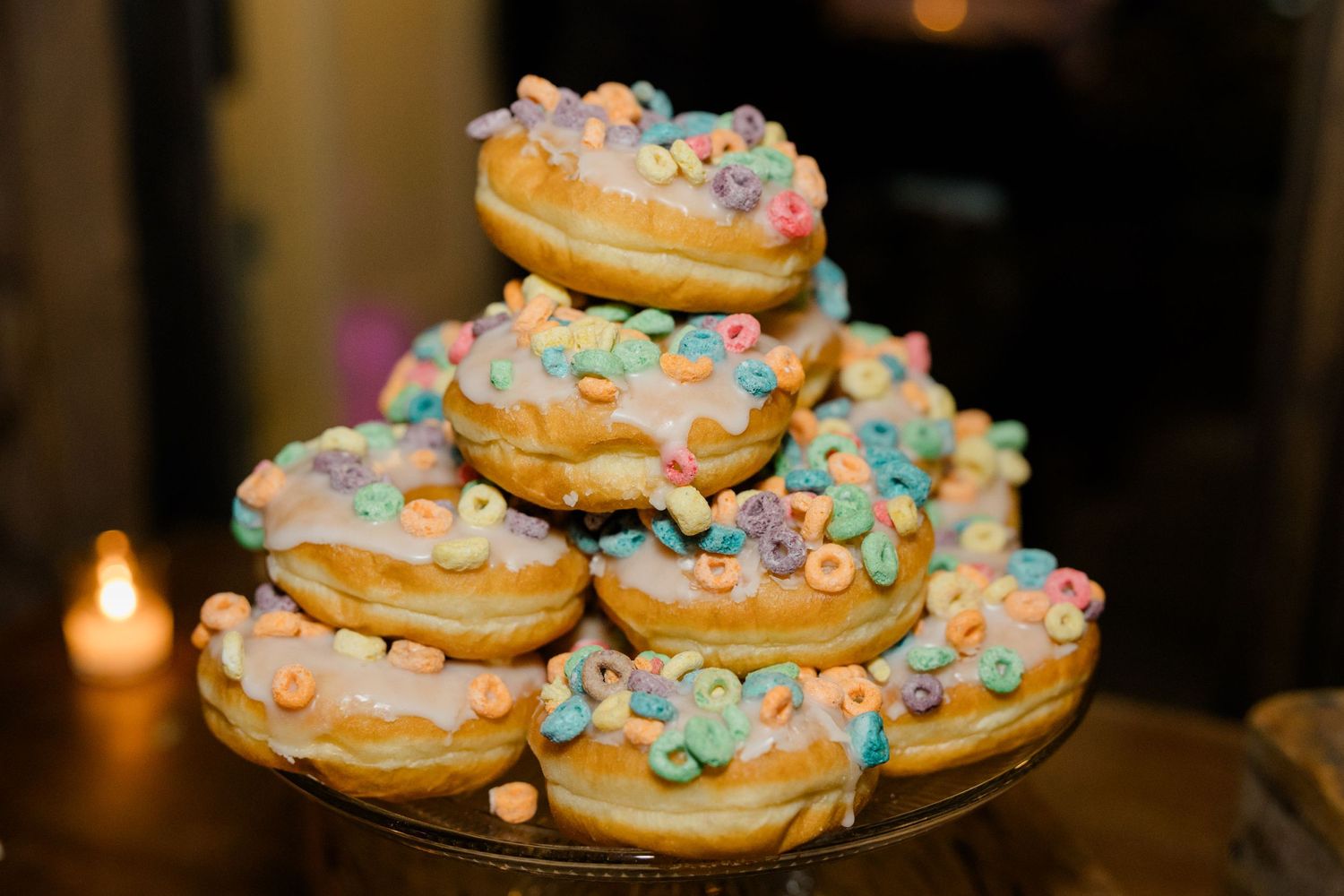Colorful frosted donuts stacked on display plate with sprinkles and pastel decorations.