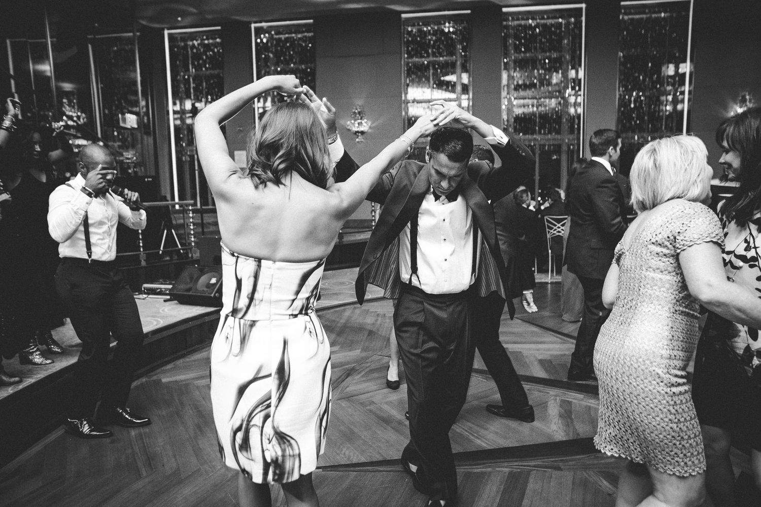 Black and white photo of wedding guests dancing at a lively reception.