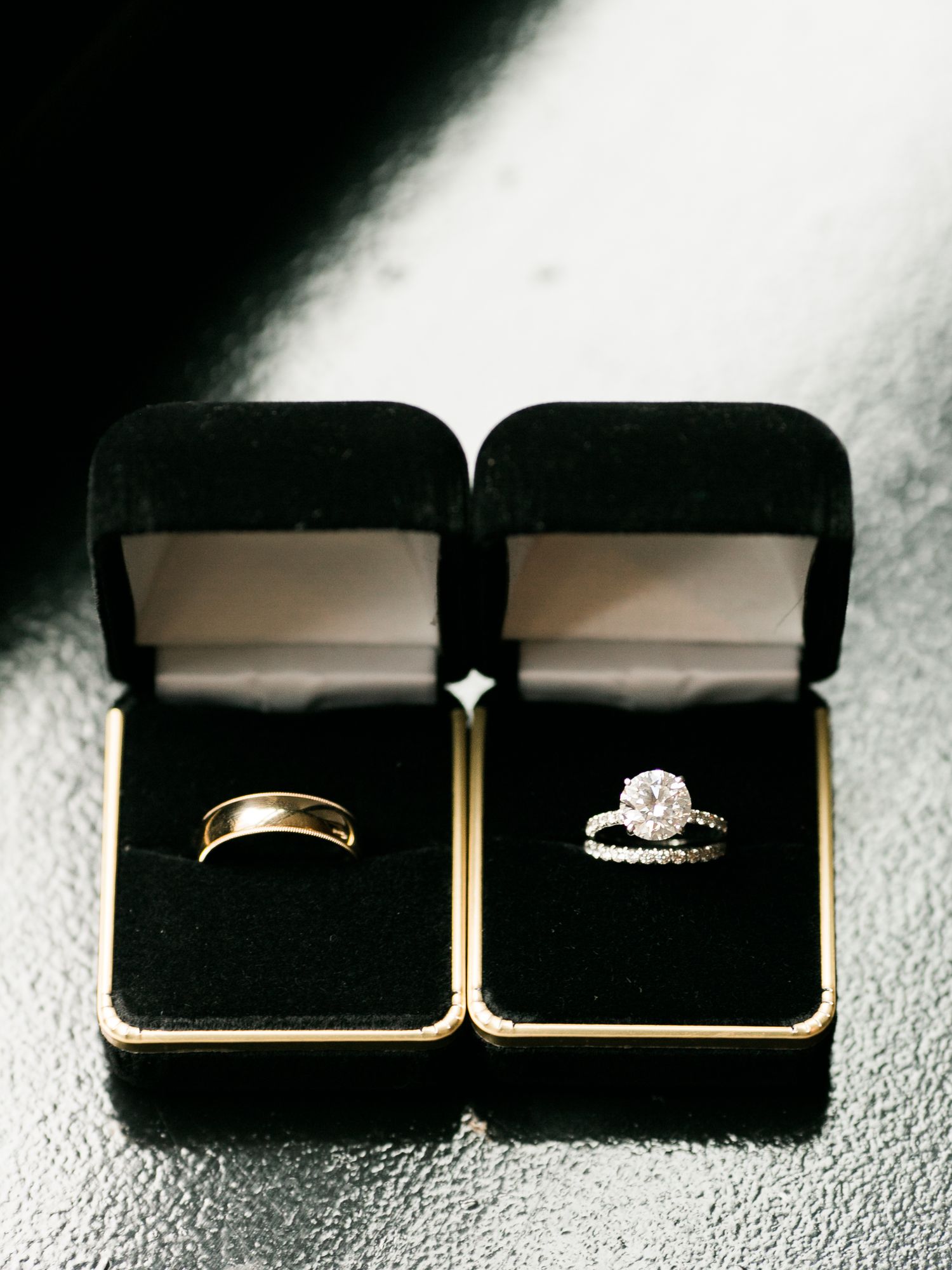 Gold wedding band and sparkling diamond engagement ring displayed in black velvet jewelry boxes.