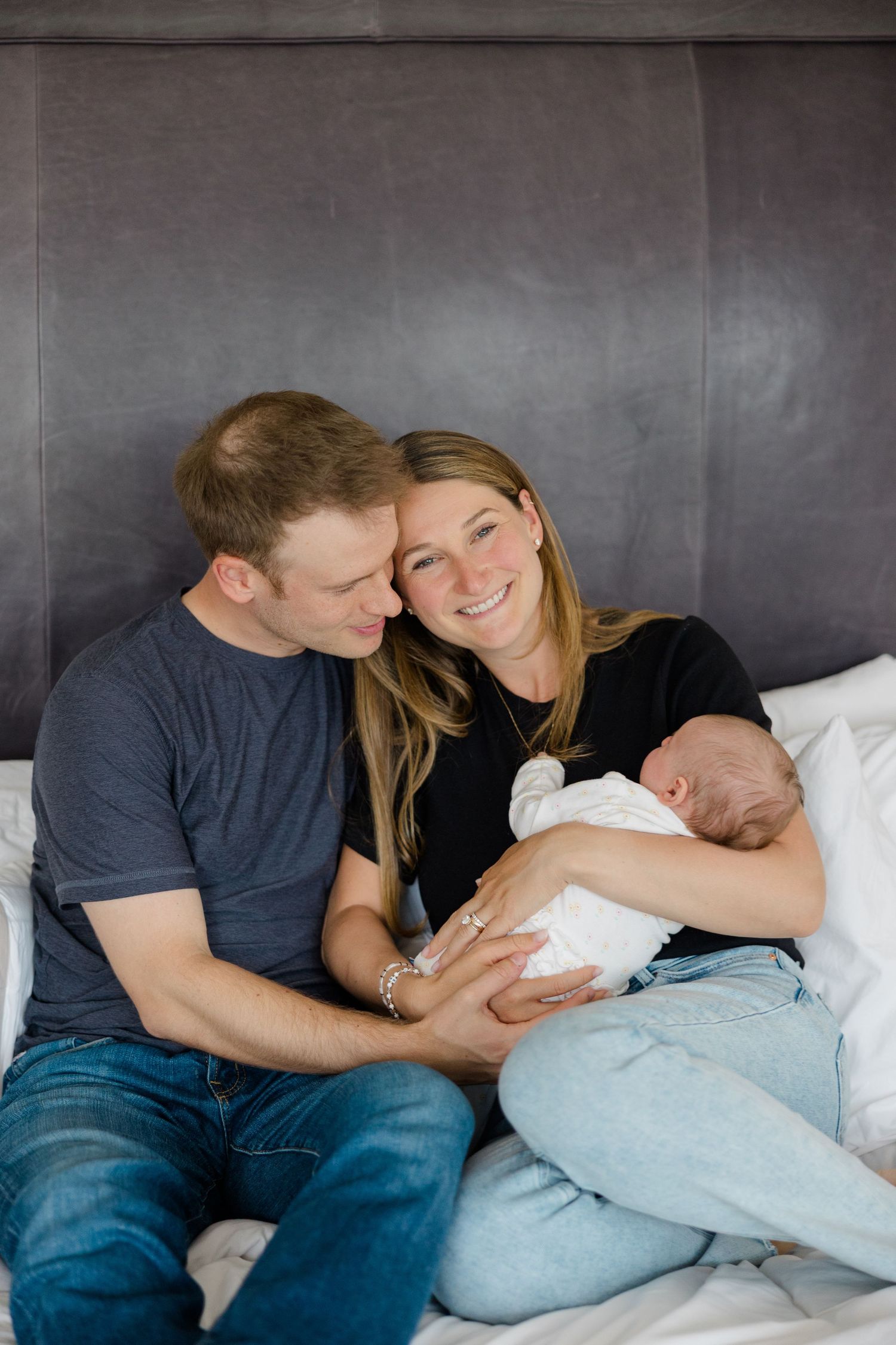 A couple cuddles with their newborn baby on a cozy gray couch.