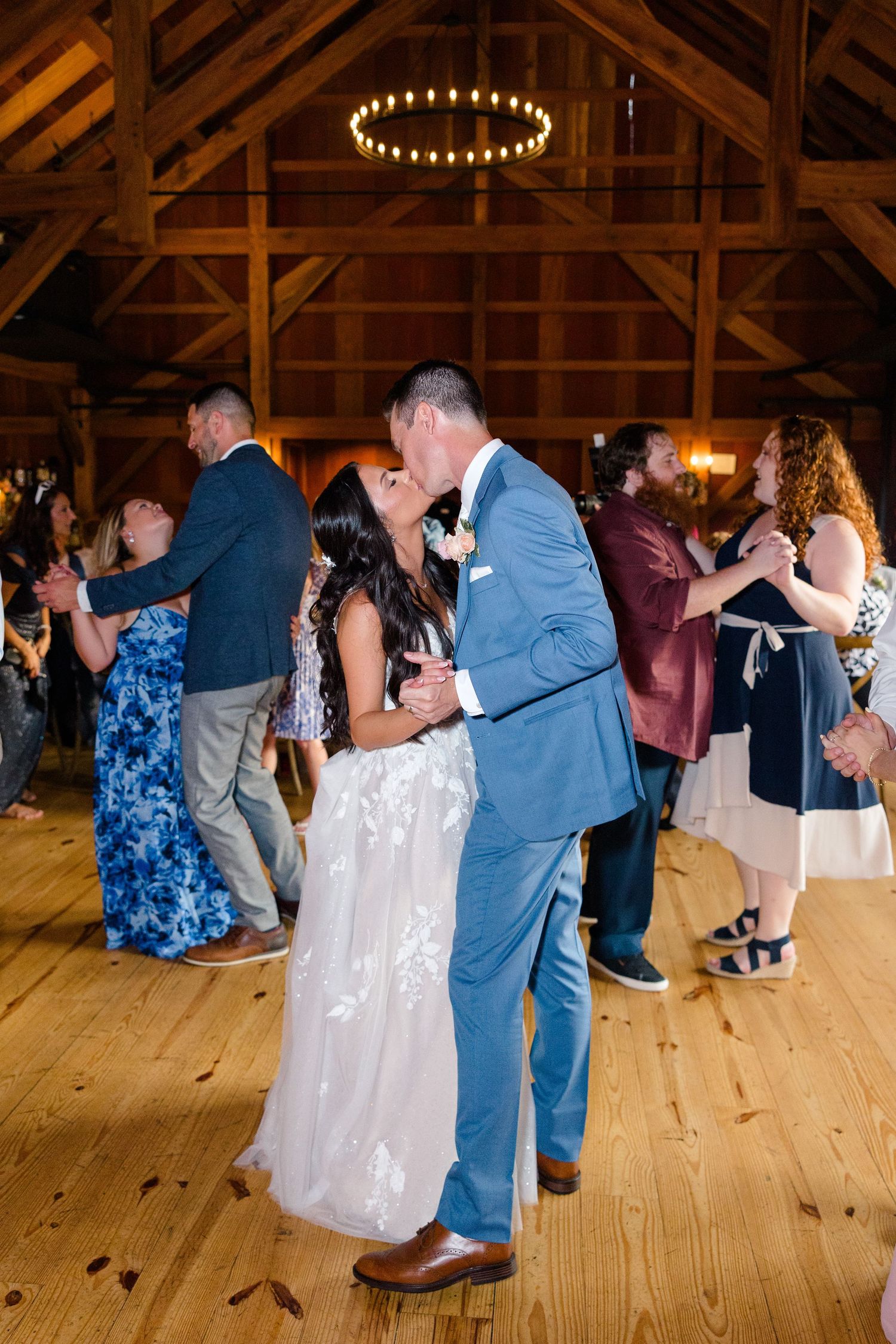 Wedding guests dancing on a wooden floor under rustic barn lighting.