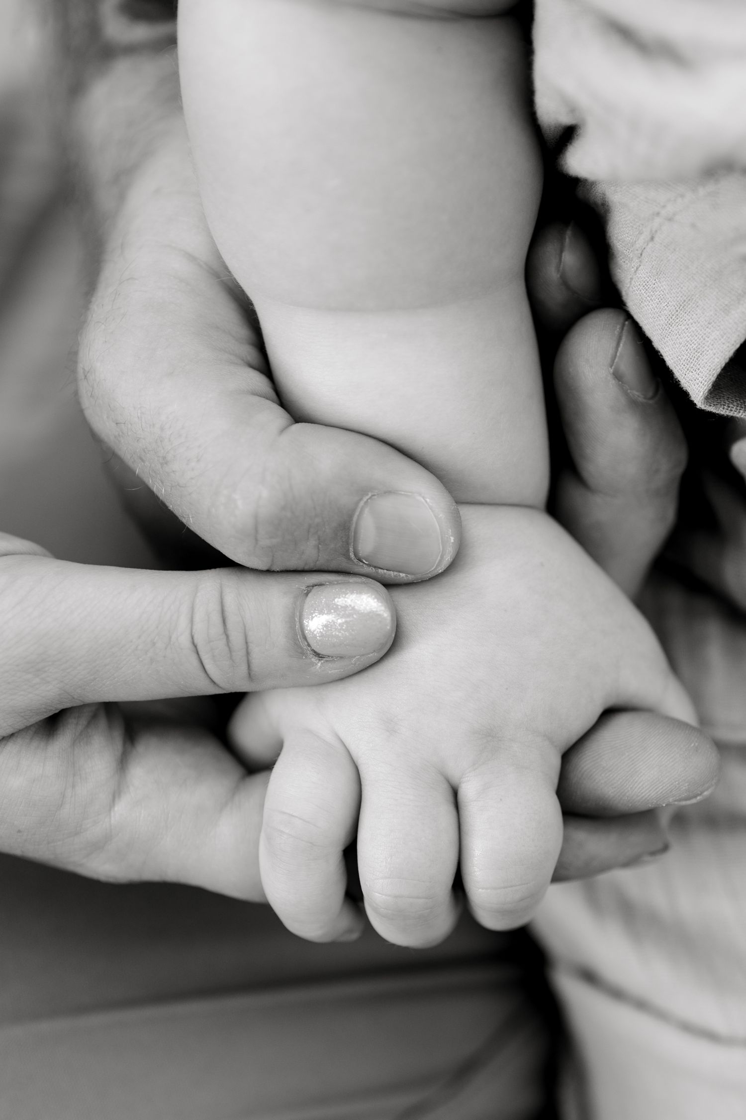 Black and white photo of an adult hand gently holding a newborn baby's tiny hand and foot.