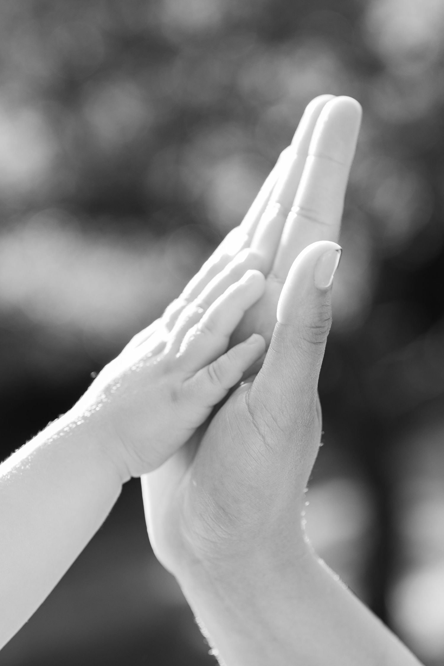 Black and white photo of a child's small hand pressing against an adult's larger hand outdoors.