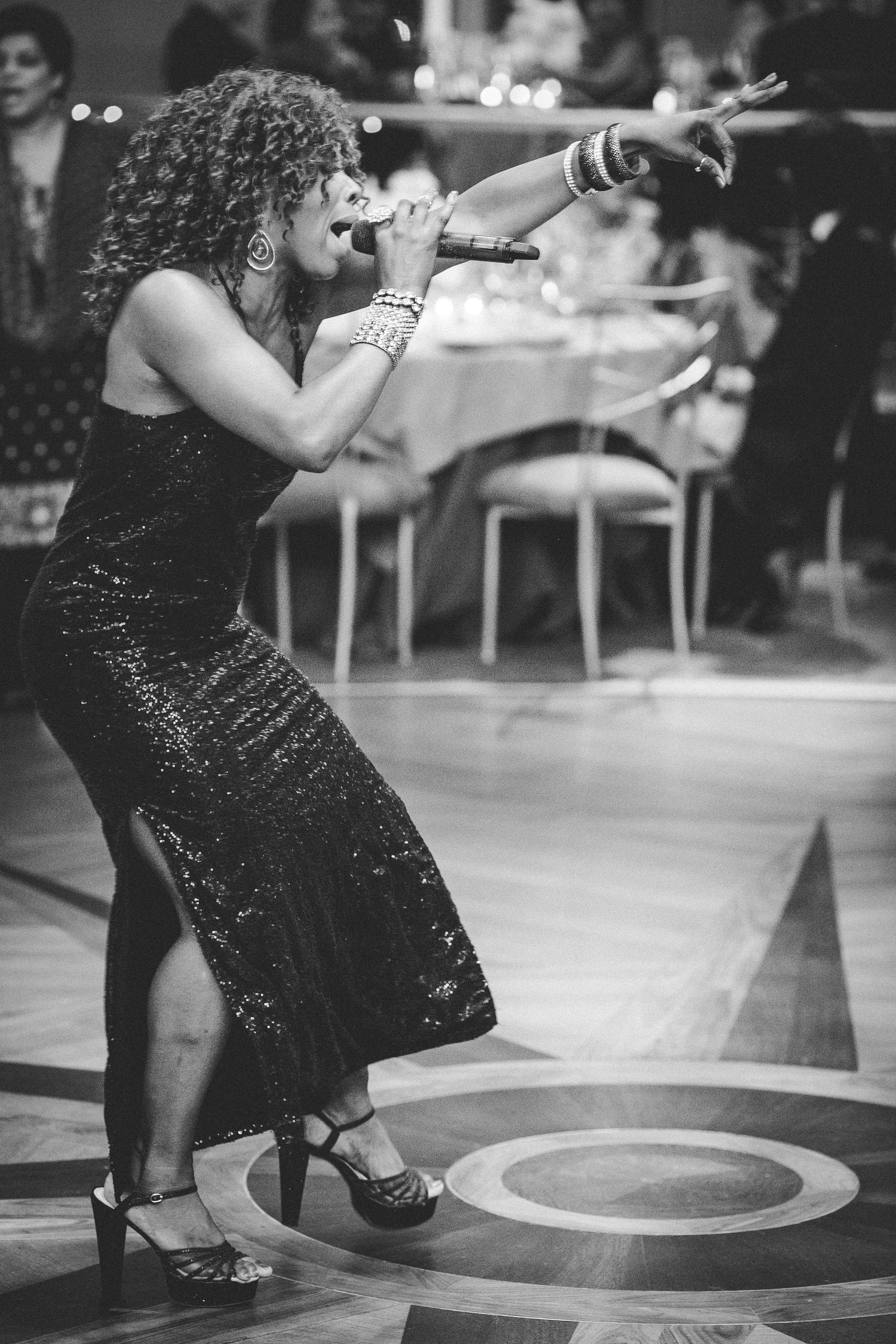 A performer in a sparkly black dress sings passionately on stage during what appears to be a vintage performance.