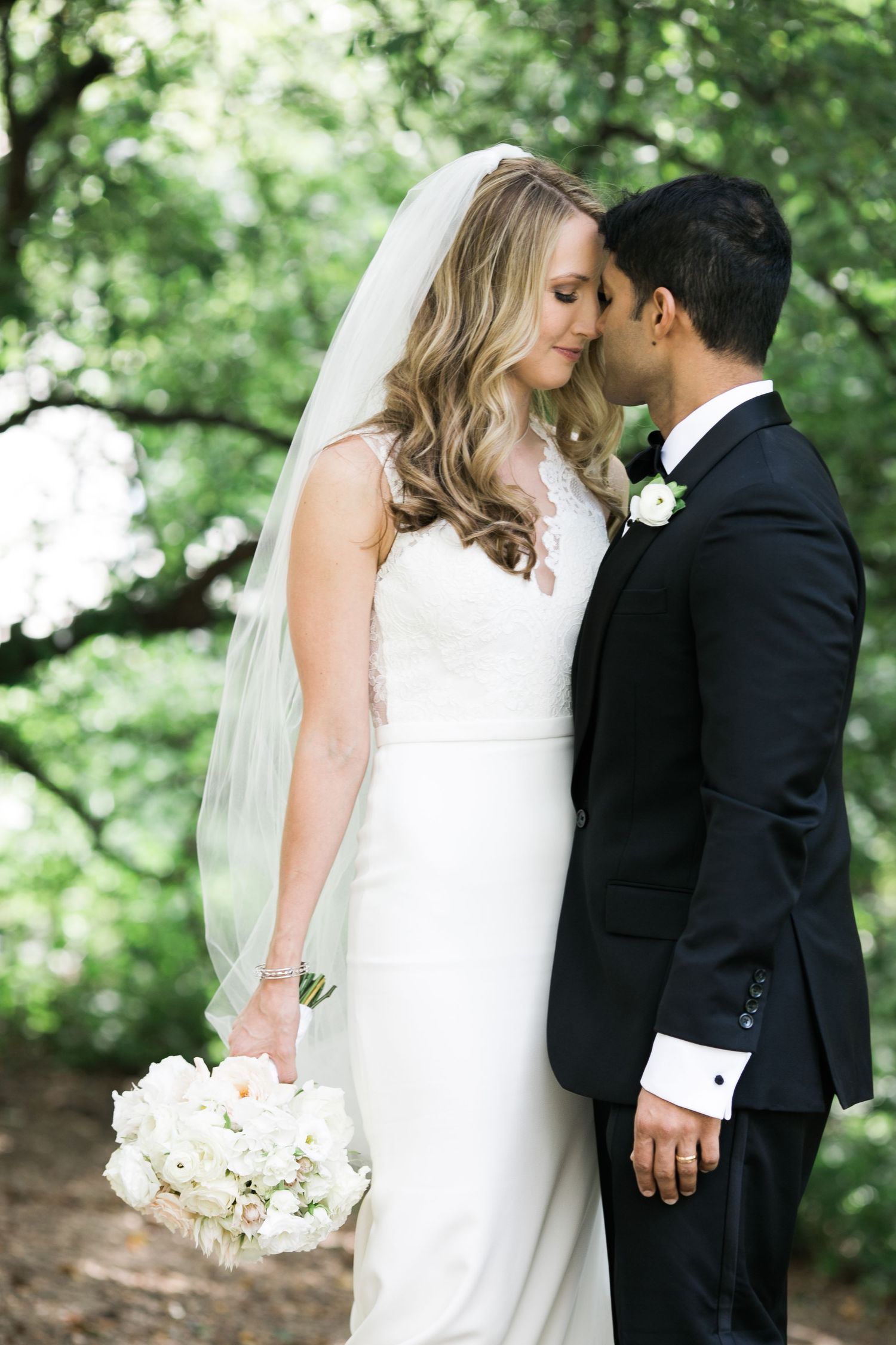 A romantic wedding photo of a couple sharing an intimate moment in a garden setting with a white bouquet.