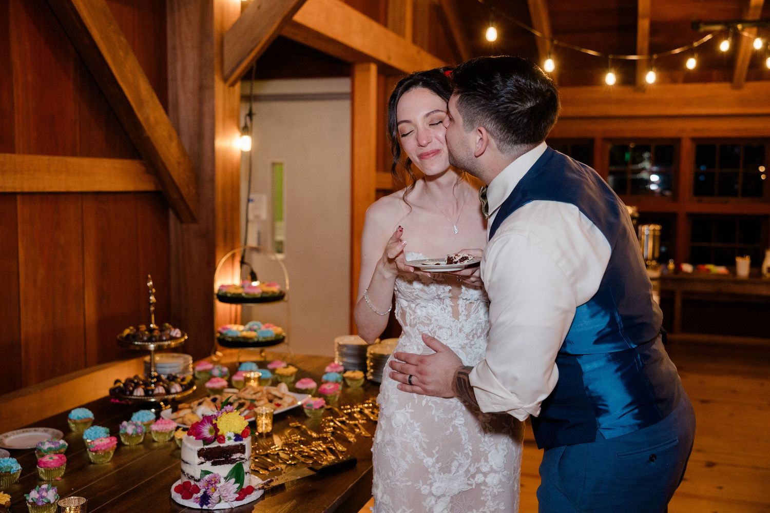 A couple shares an intimate moment at their rustic barn wedding reception dessert table.