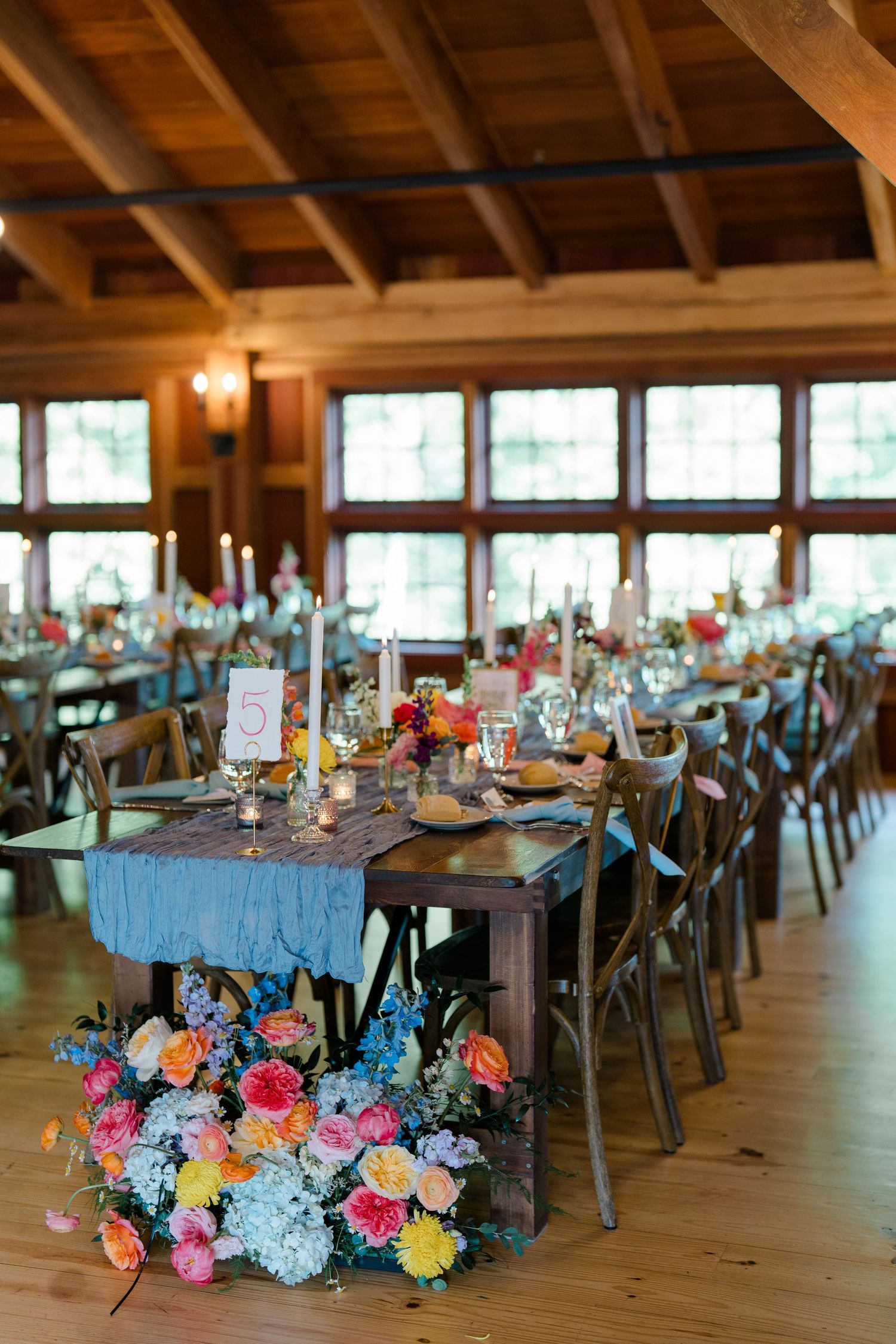 Rustic wedding reception venue with wooden beams and colorful floral arrangements on long dining tables.