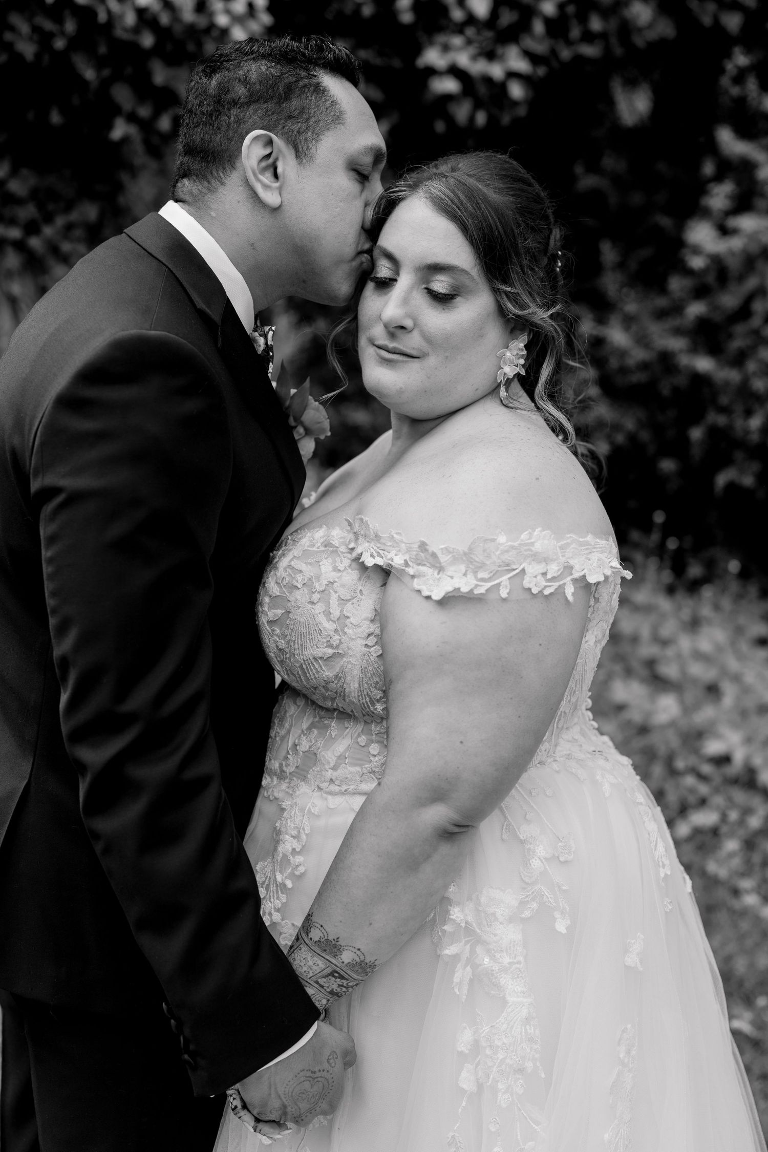 Intimate black and white wedding portrait capturing a tender moment between newlyweds in formal attire.