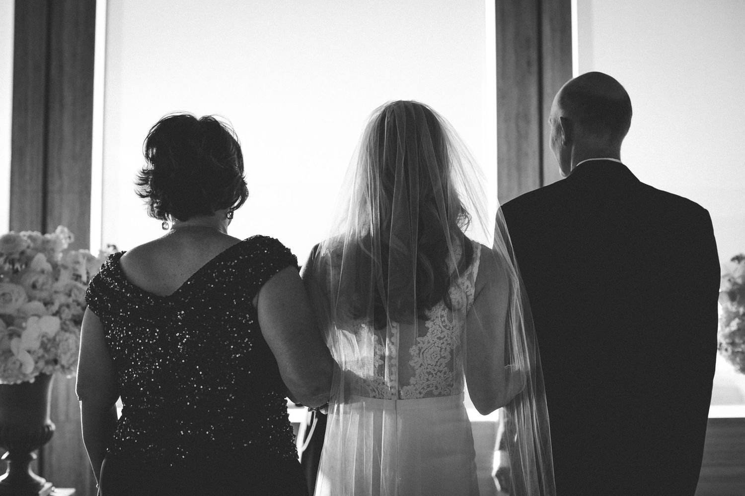 Silhouette of three people looking out window at wedding celebration.