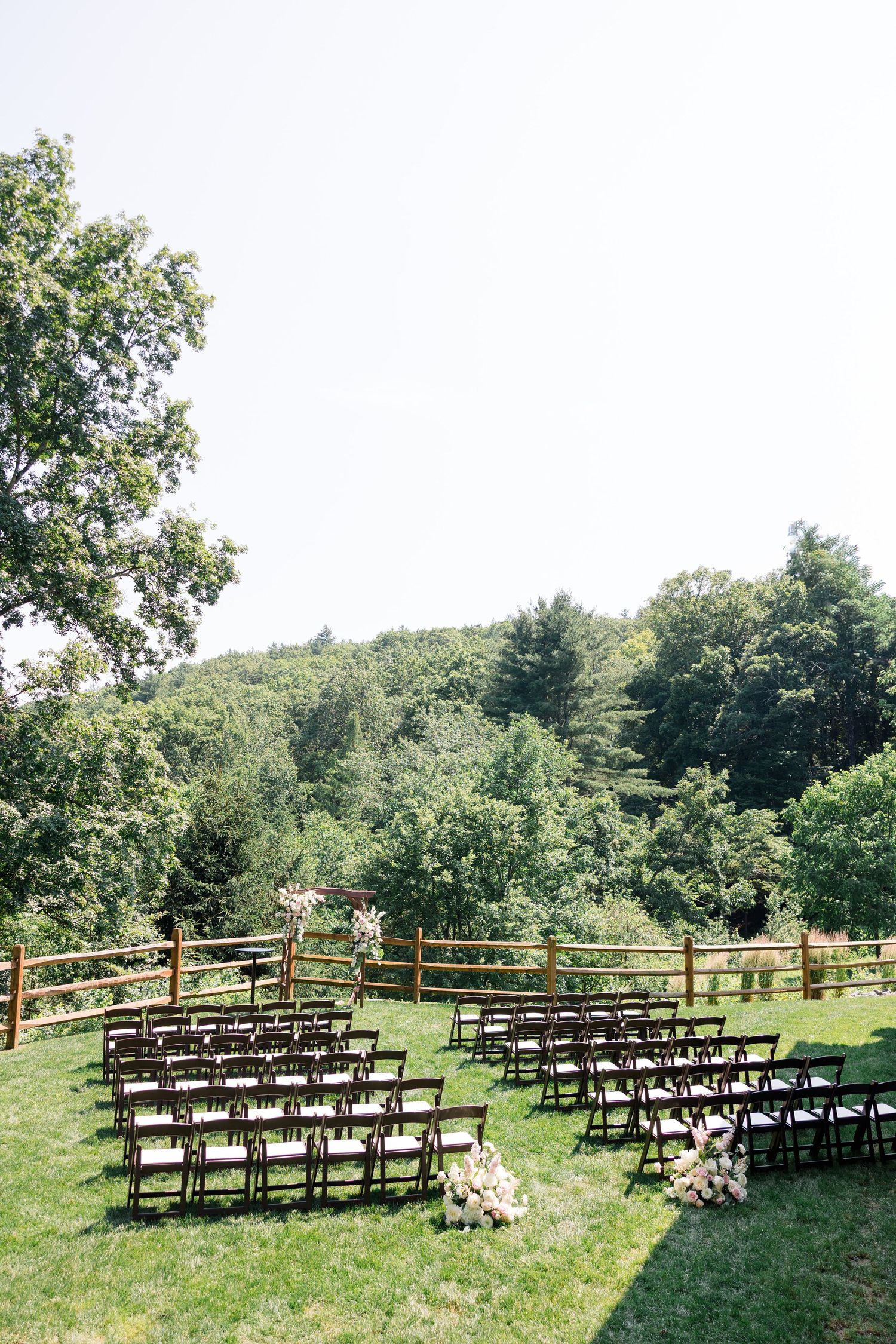 Outdoor wedding ceremony setup with wooden chairs arranged on a hillside under trees.