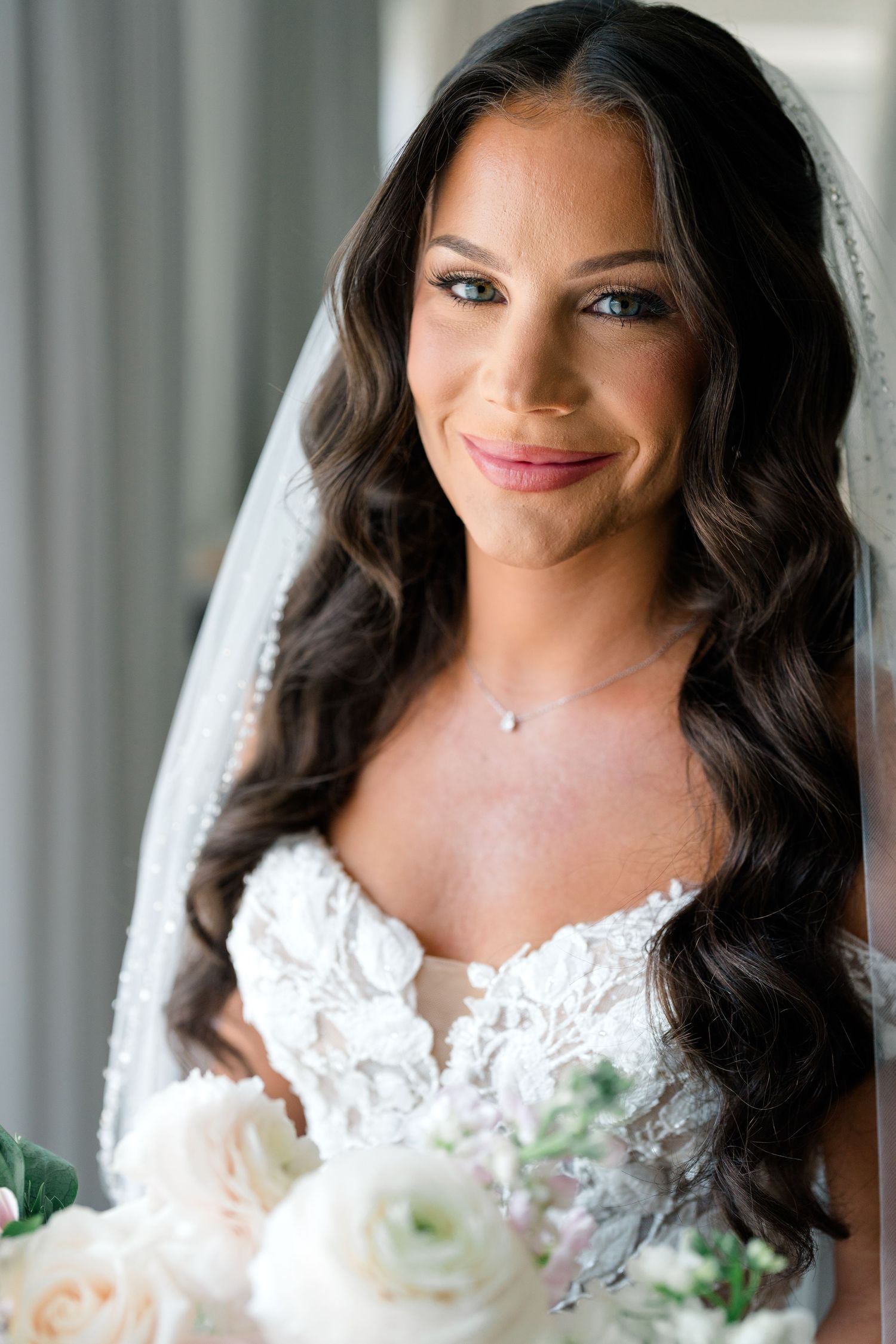 Close up portrait of bride in white lace dress holding white roses.