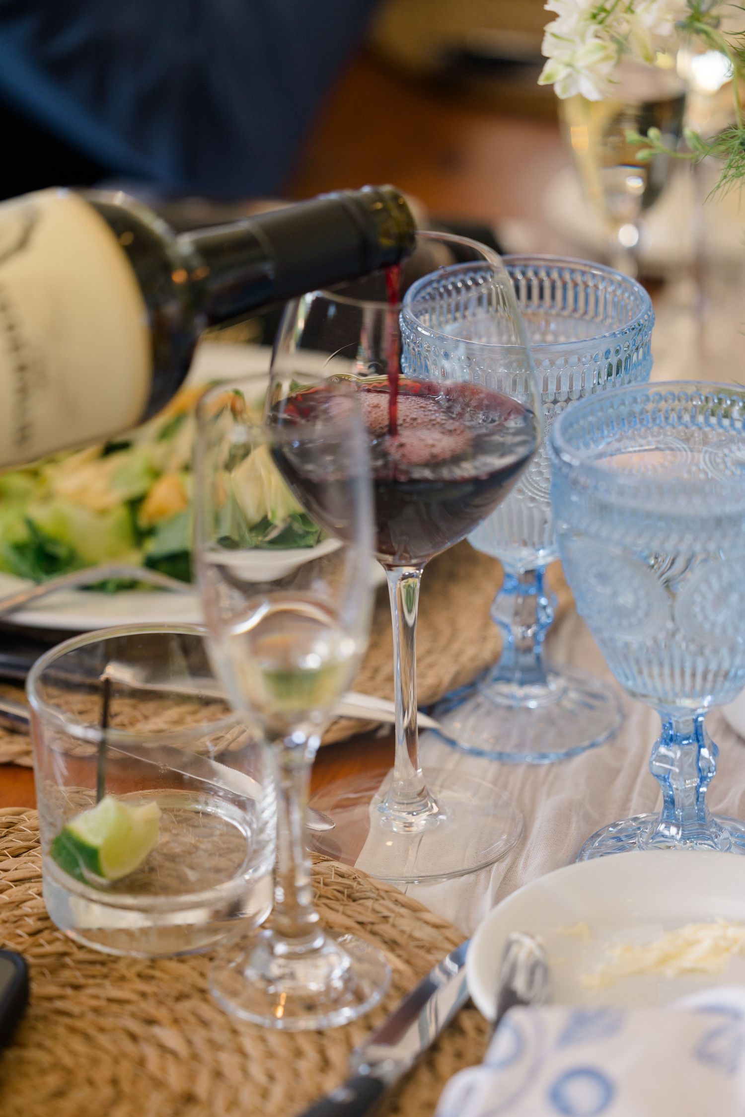 Red wine being poured into glass at elegantly set wedding reception table with blue glassware.