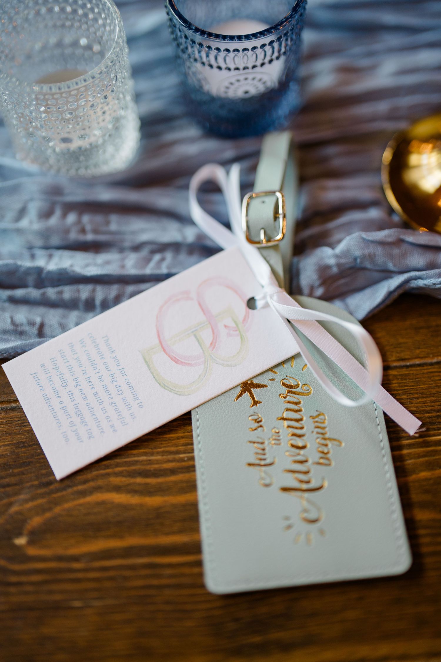 Wedding invitation cards with calligraphy and rings design tied with white ribbon, displayed on wooden surface.