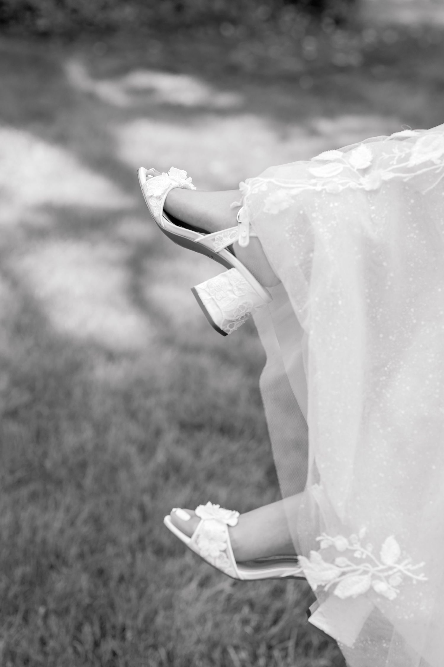 Black and white detail shot of bride's feet in delicate shoes under wedding dress hem.