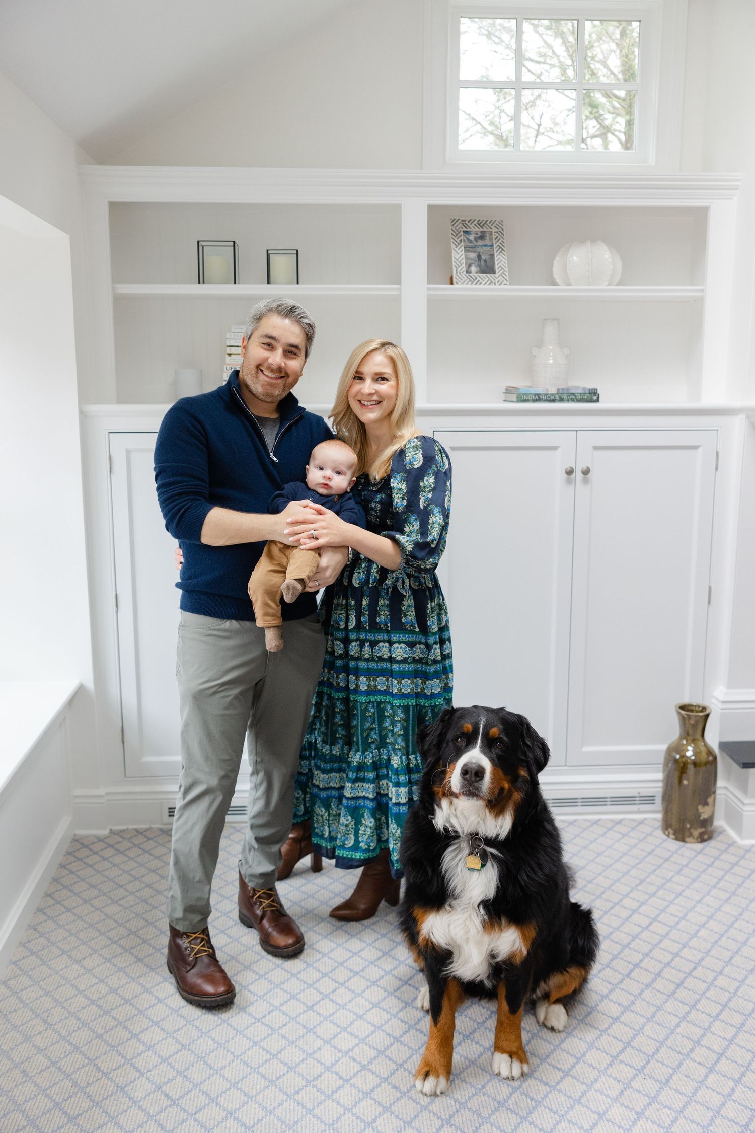 A couple poses with their Bernese Mountain Dog in a bright white modern room with tile flooring.