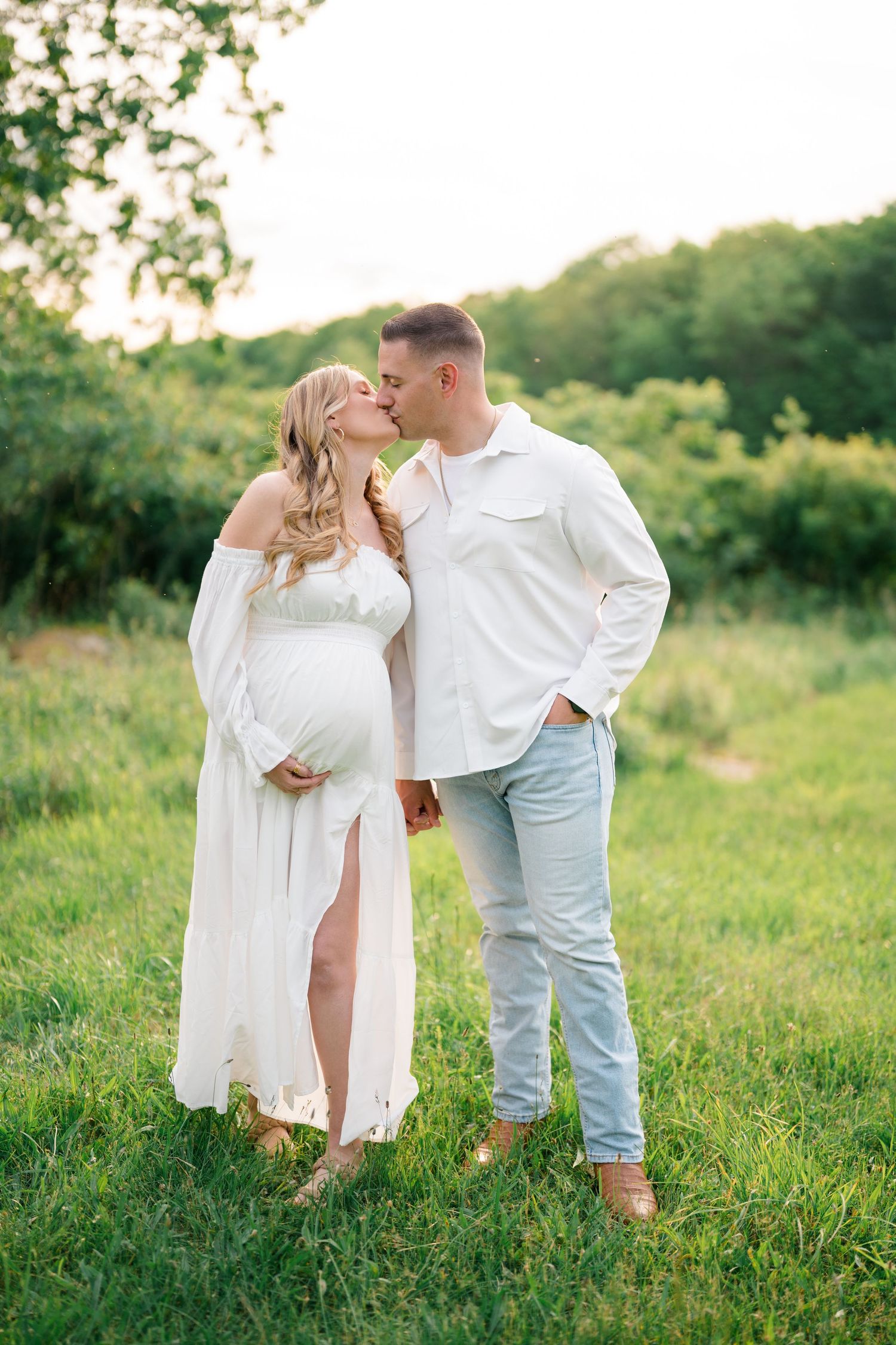 Romantic couple in white clothing embracing in a sunny green meadow.
