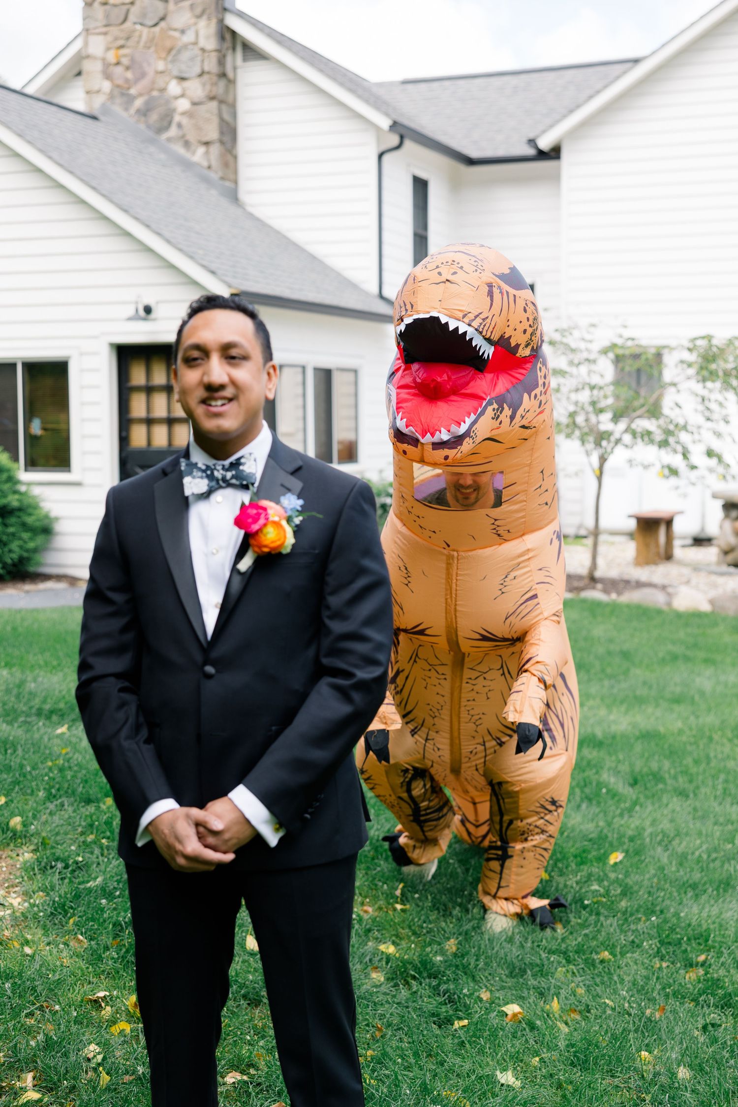 Wedding photoshoot featuring someone in a tuxedo with a partner wearing an inflatable T-Rex costume.
