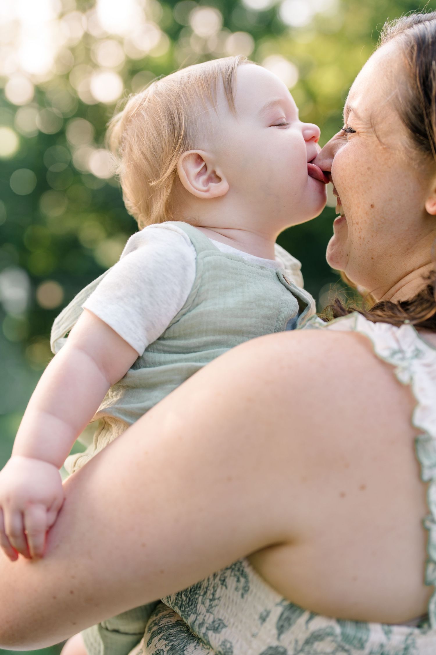 Adorable baby boy giving mom a slobbery kiss on the cheek during outdoor photo session.