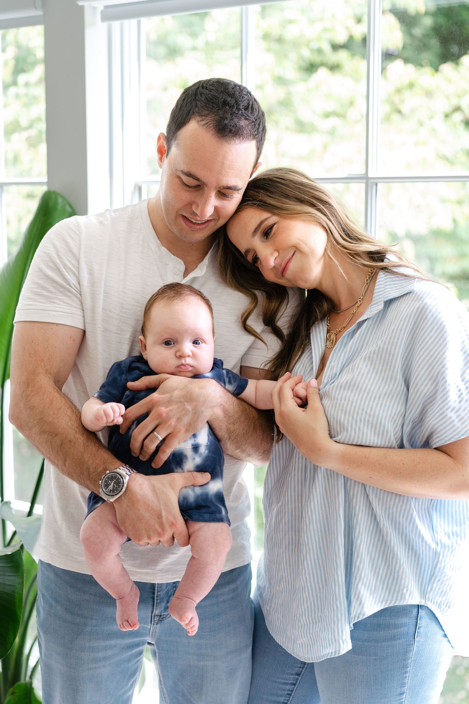 A loving family shares a tender moment together by a bright window with their baby in casual attire.