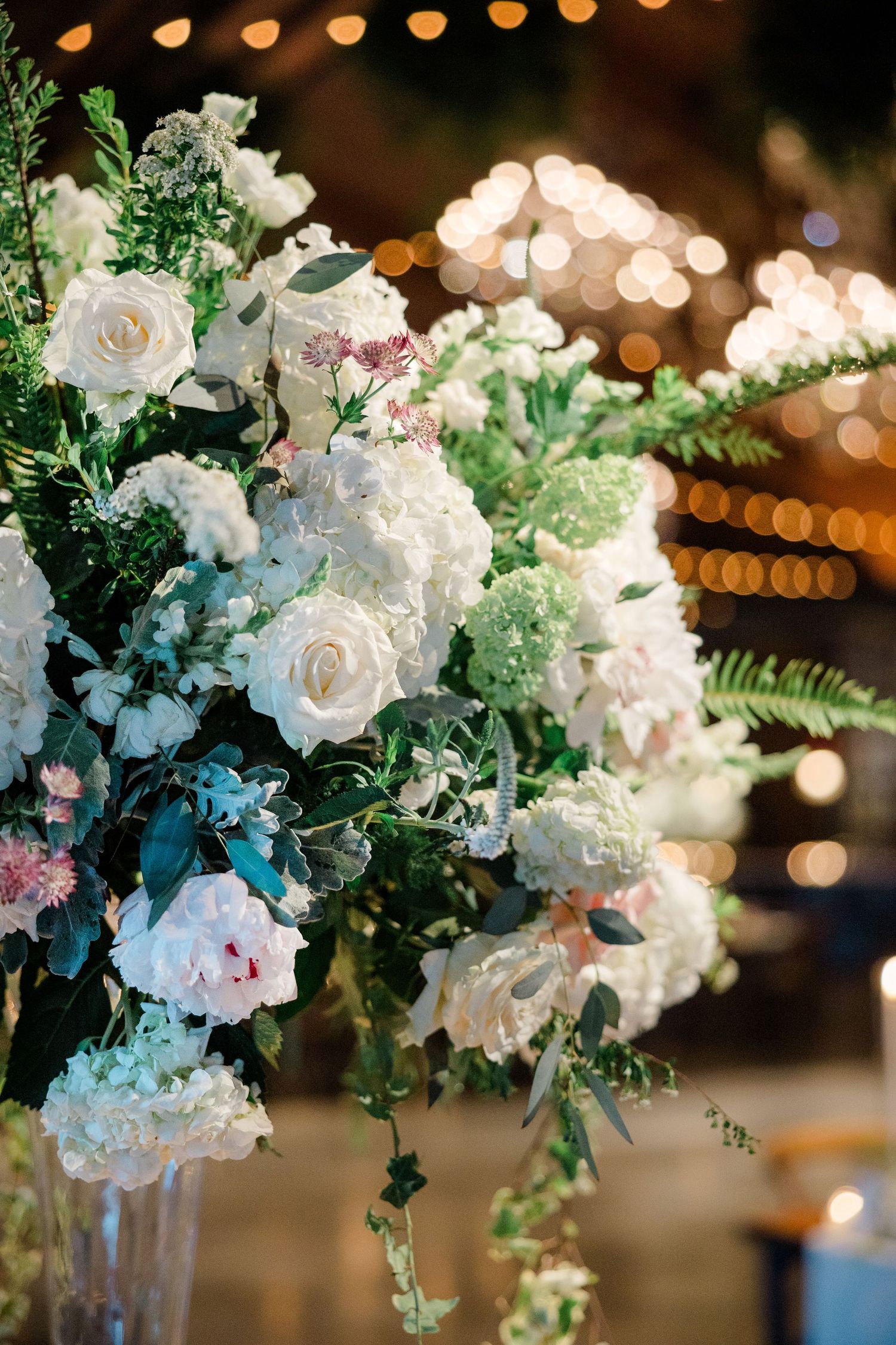Luxurious wedding floral arrangement with white roses and greenery against soft bokeh lights.