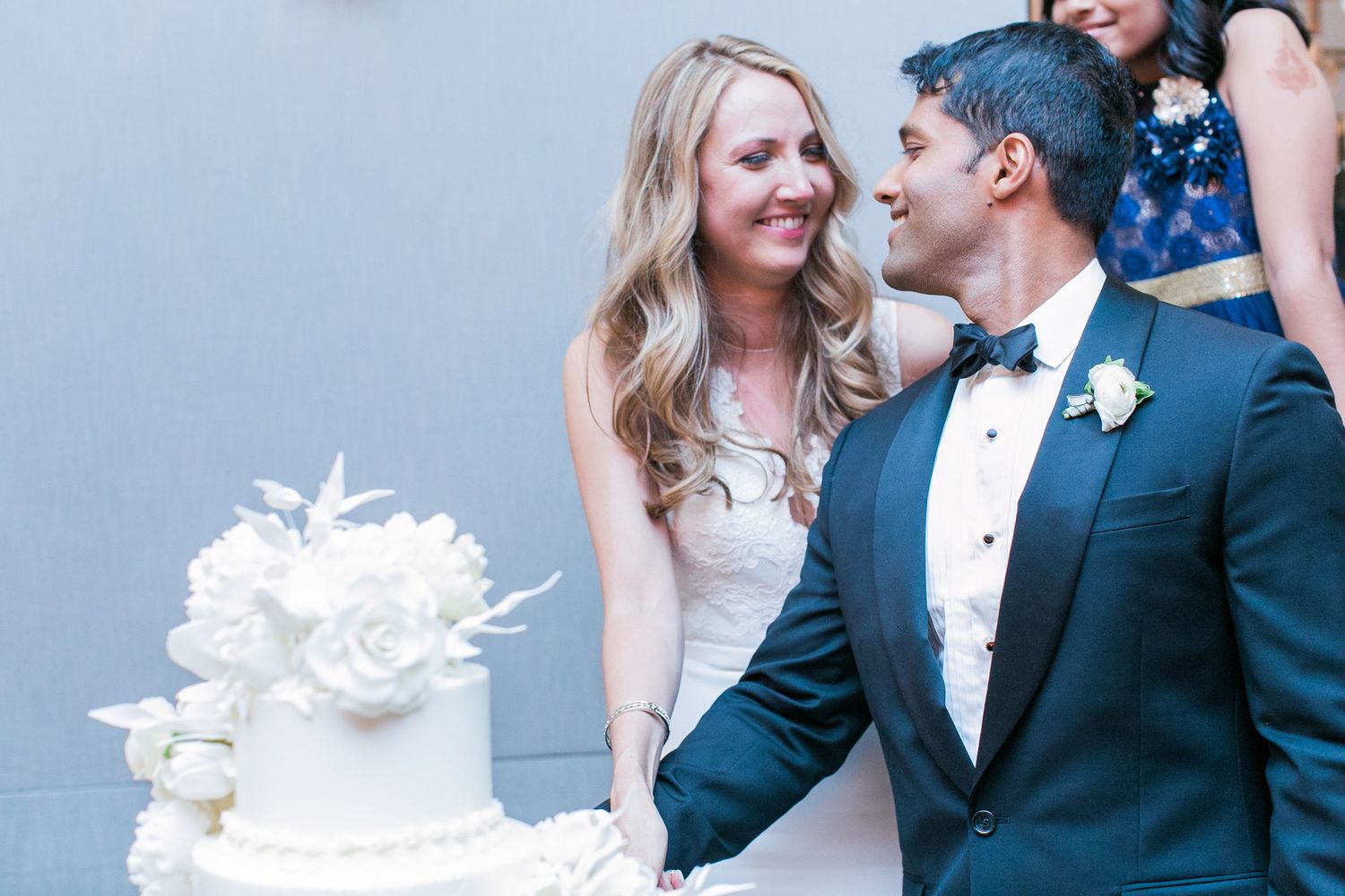 Elegant wedding couple sharing a joyful moment beside their white wedding cake.