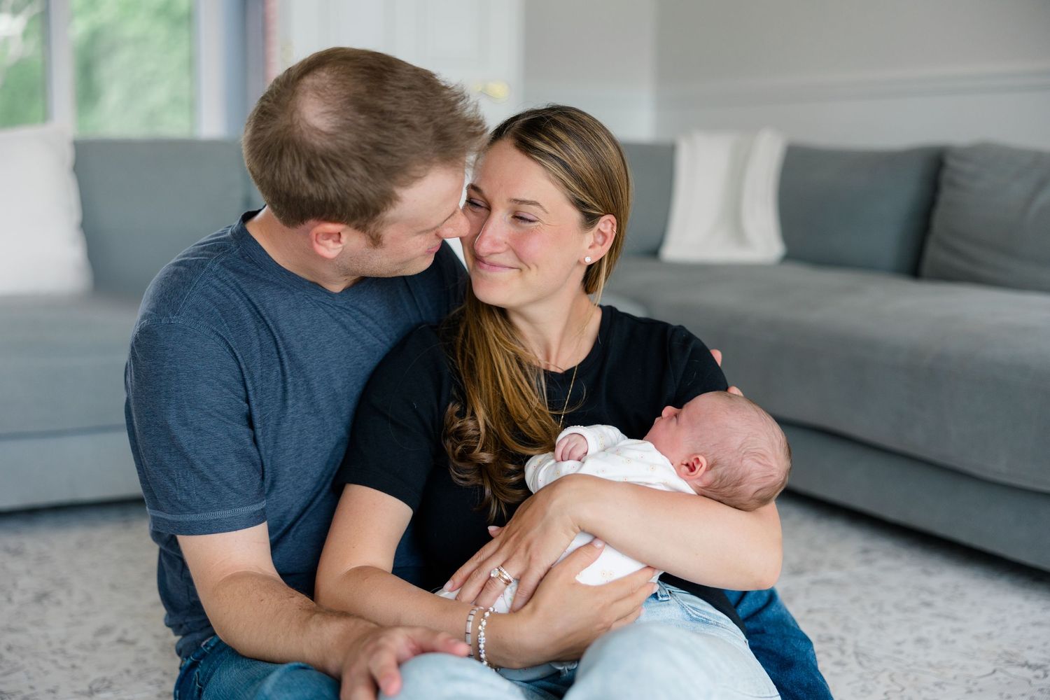 Family members sharing tender moments with a newborn baby on a living room floor.