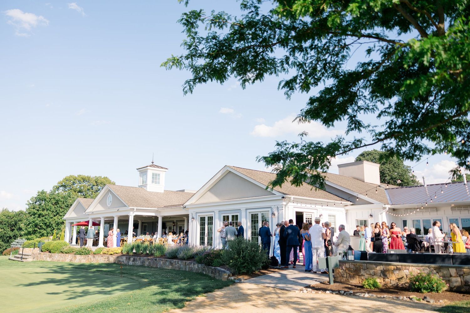 Elegant white country club venue surrounded by manicured grounds filled with colorful wedding guests.