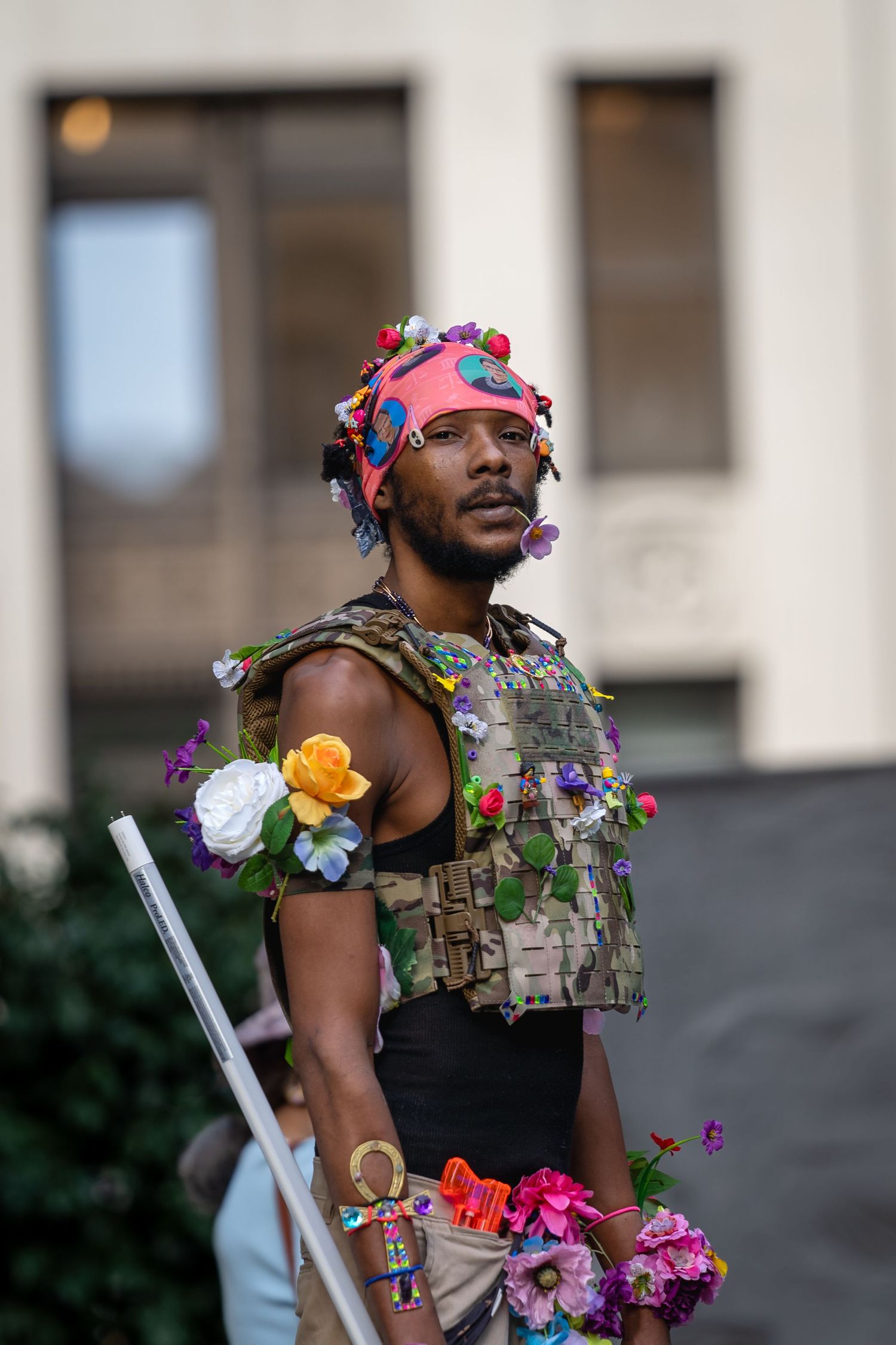Performer wearing colorful floral decorations and tactical vest during an artistic performance.