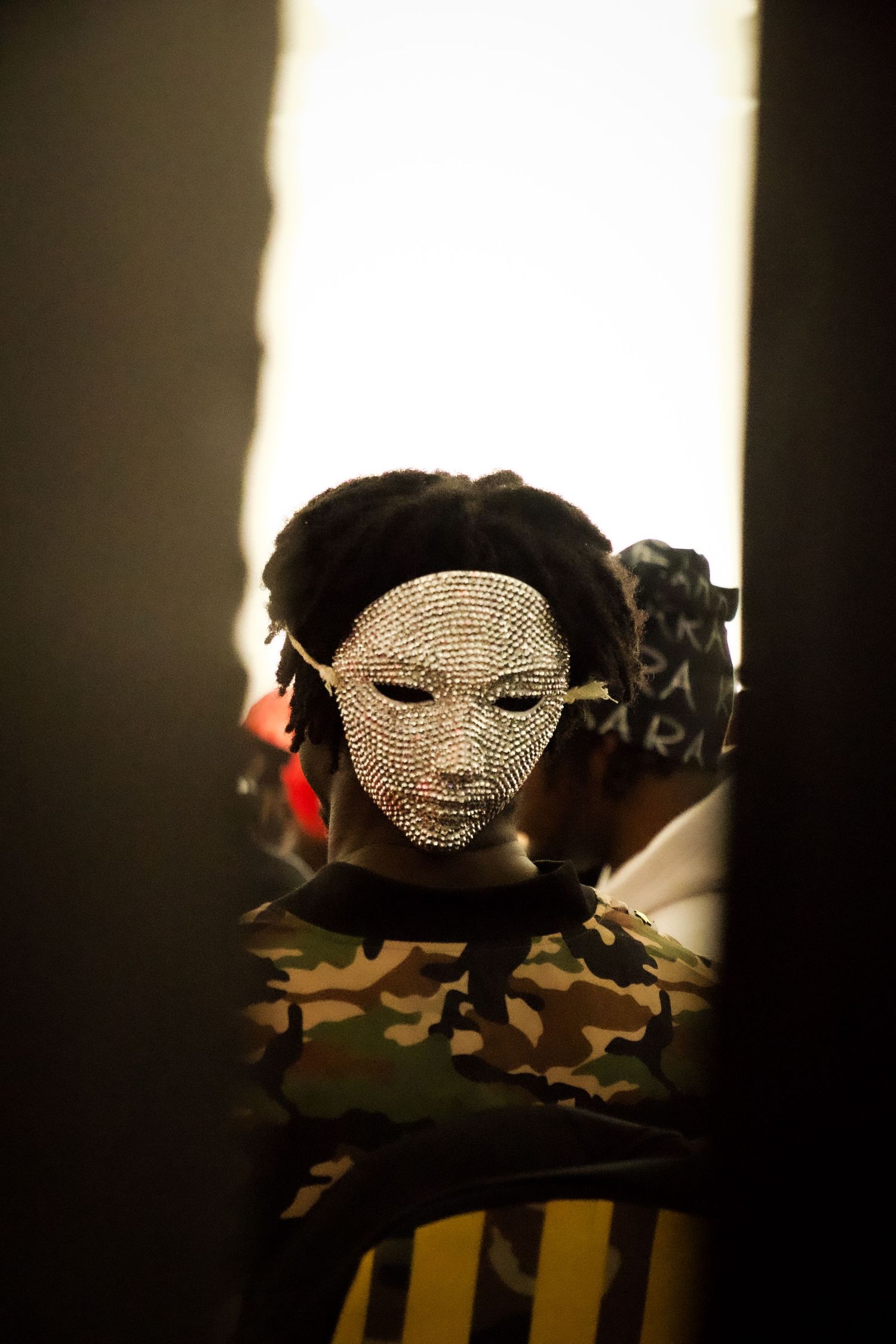Artistic silhouette wearing sparkly mask in dramatic lighting.
