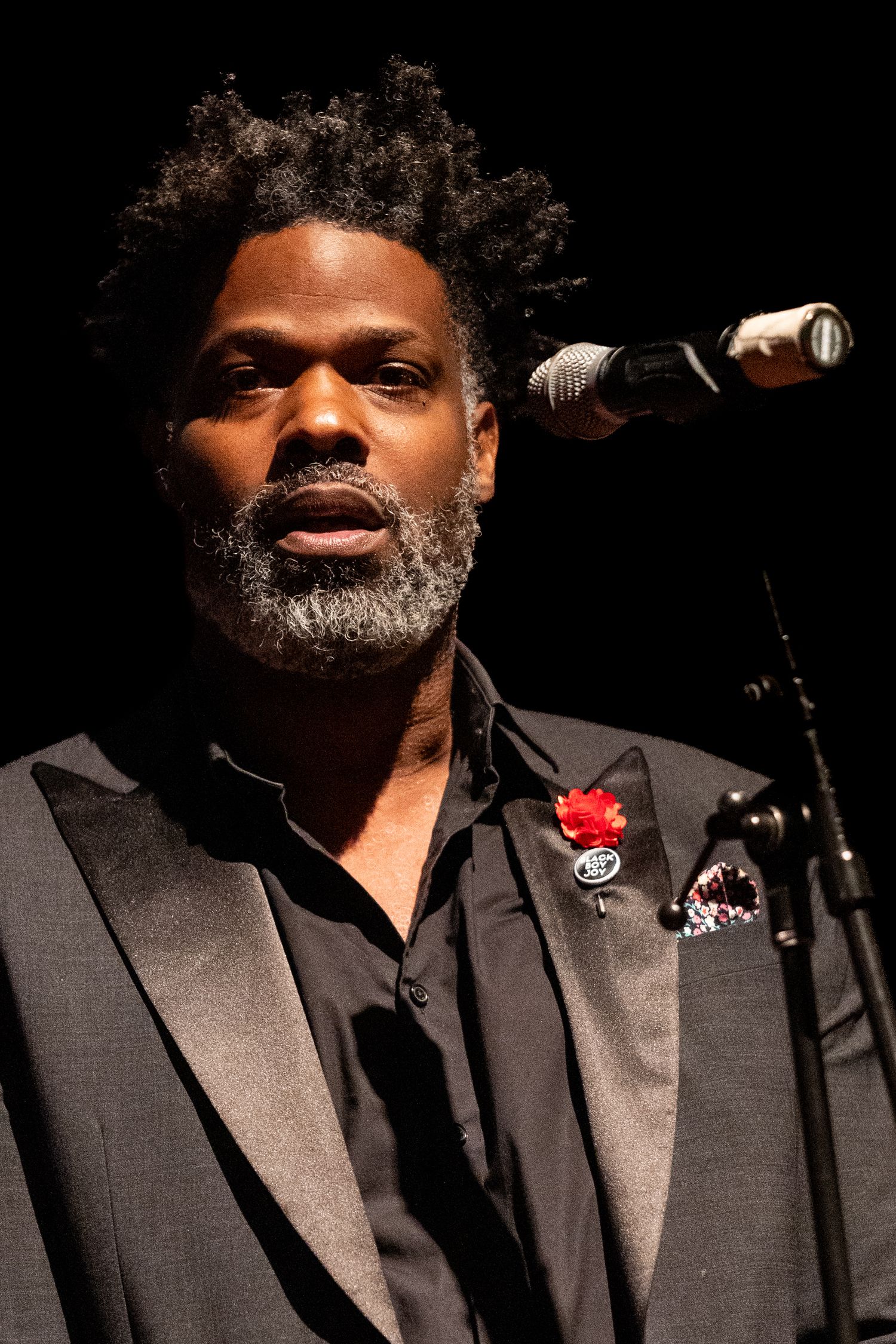 Singer in dark suit performing on stage with dramatic lighting.