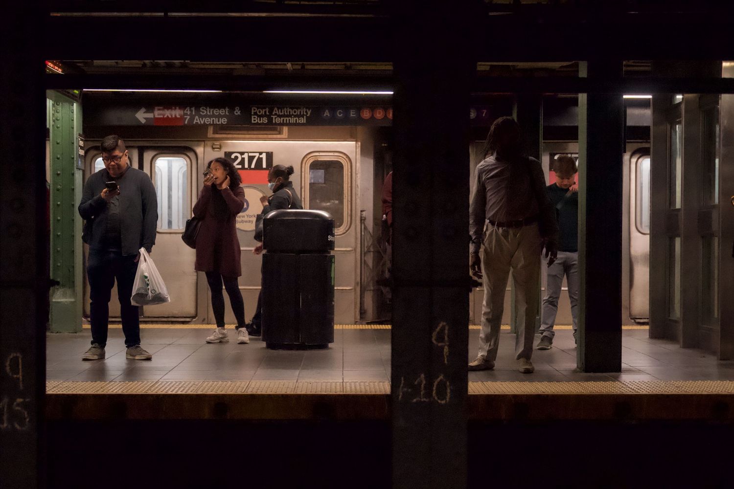 Silhouettes of commuters waiting on dark subway platform.