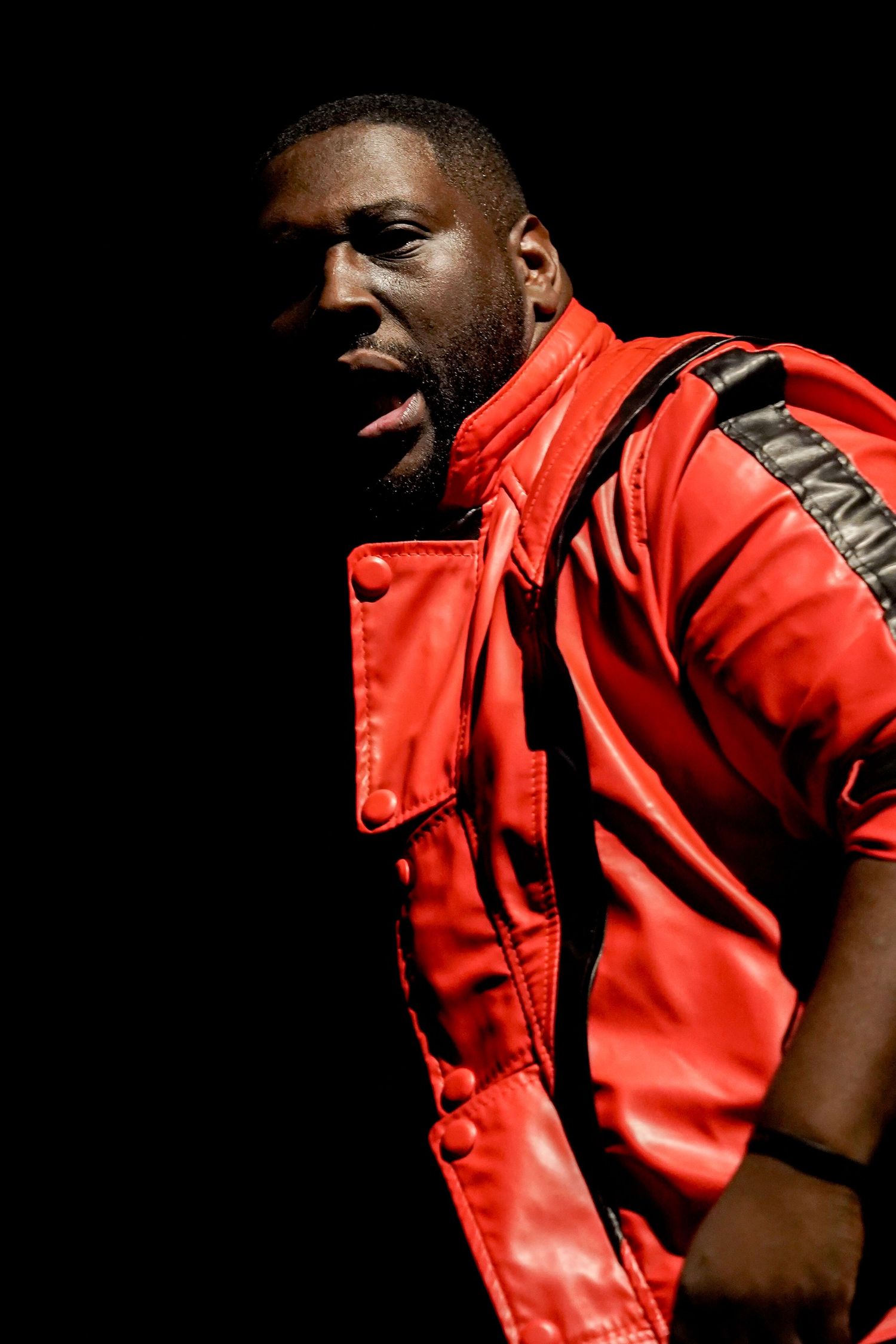 Dramatic side view of person wearing bright red jacket against black background.