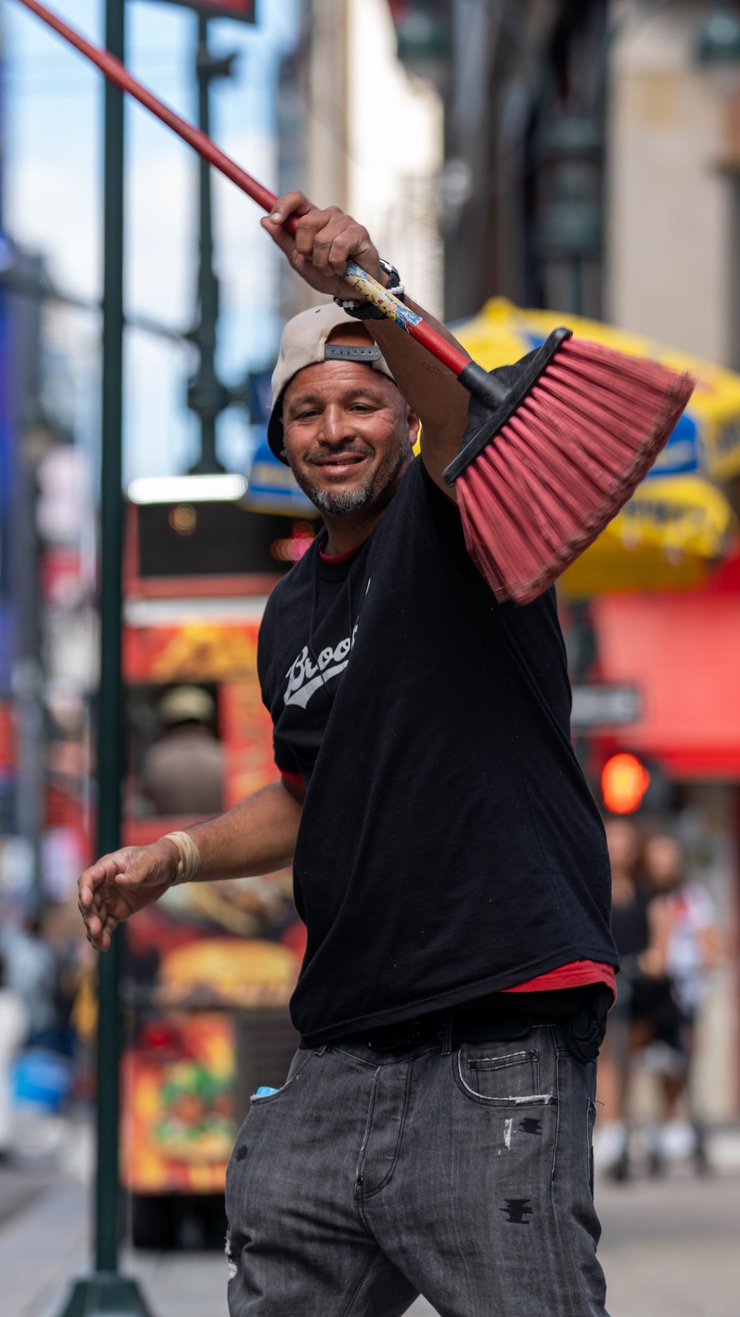 A person in black clothing dances with a red fan on a city street.