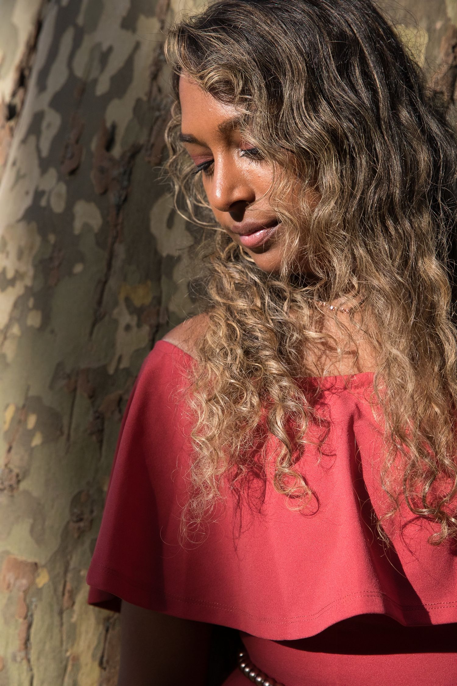 Portrait series showing curly hair and red top against textured wall background.