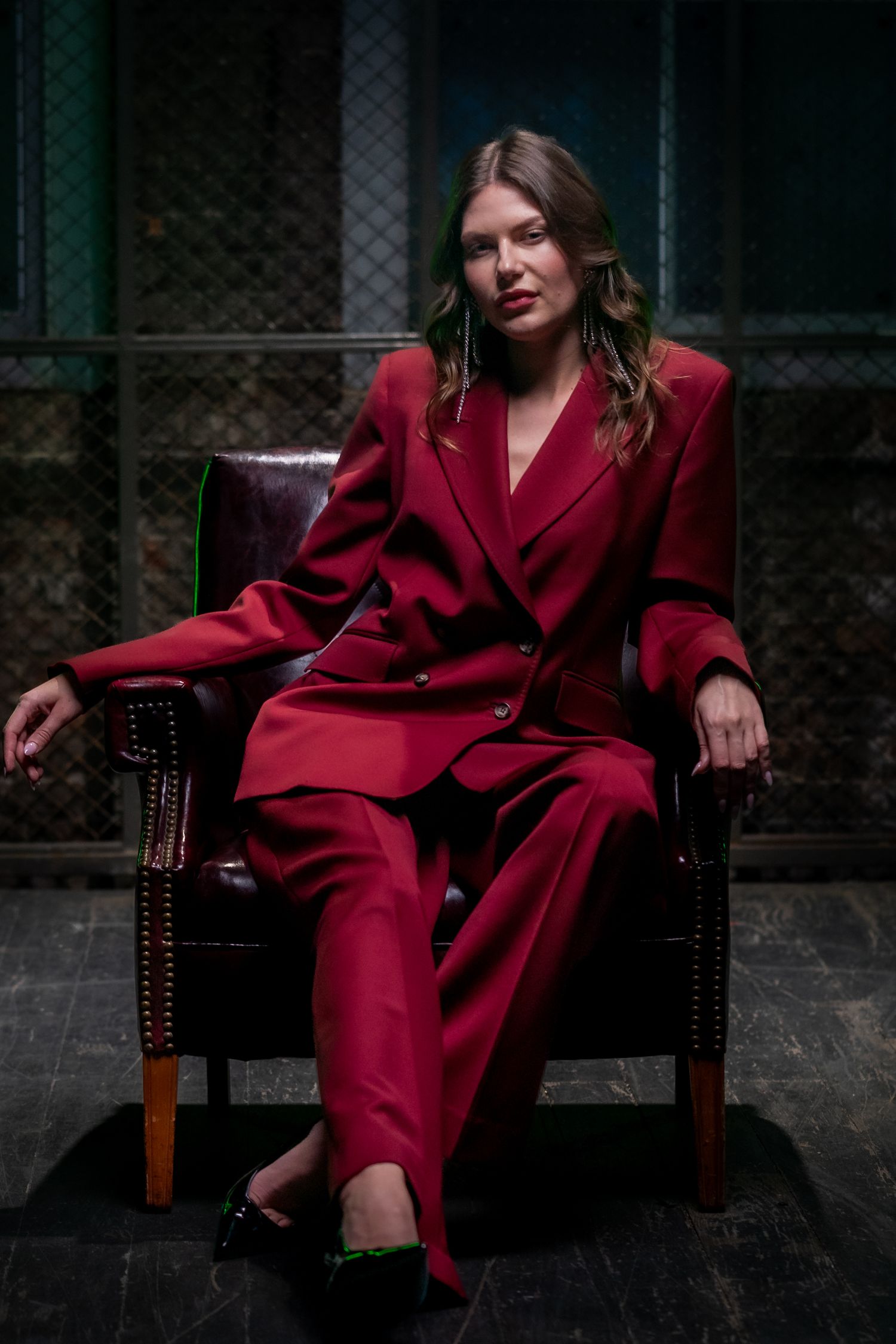 Figure in a striking red suit lounges dramatically across a dark leather chair.