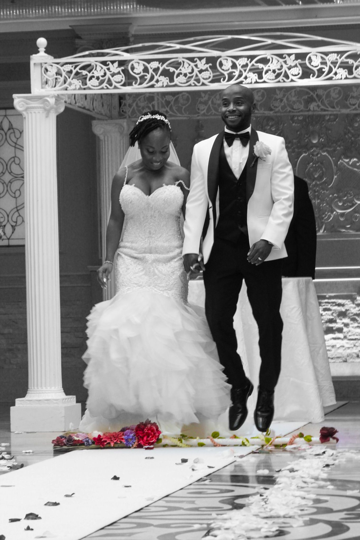 Black and white wedding photo showing couple walking down decorated aisle.