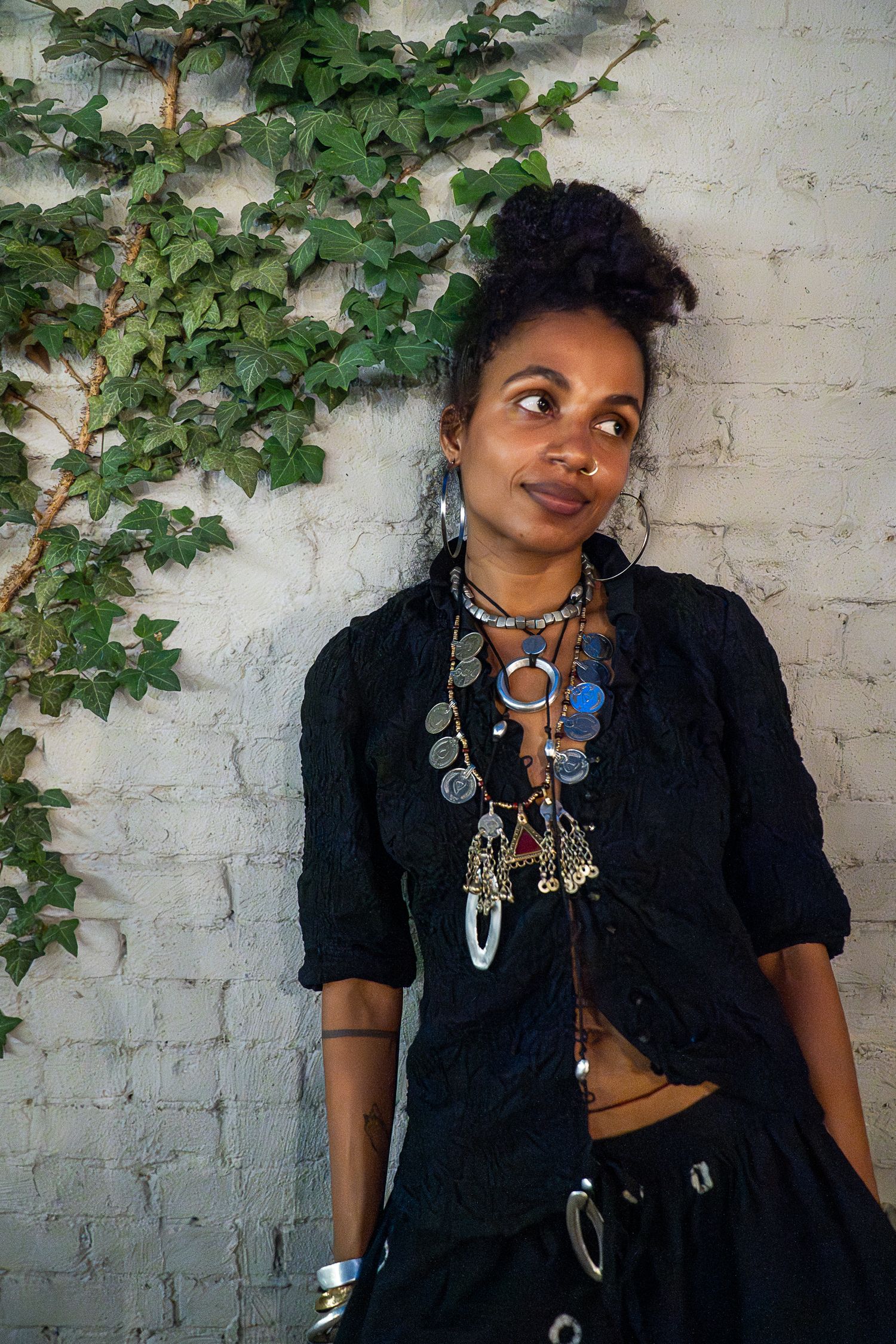 Portrait against white brick wall with climbing ivy and ornate jewelry details.