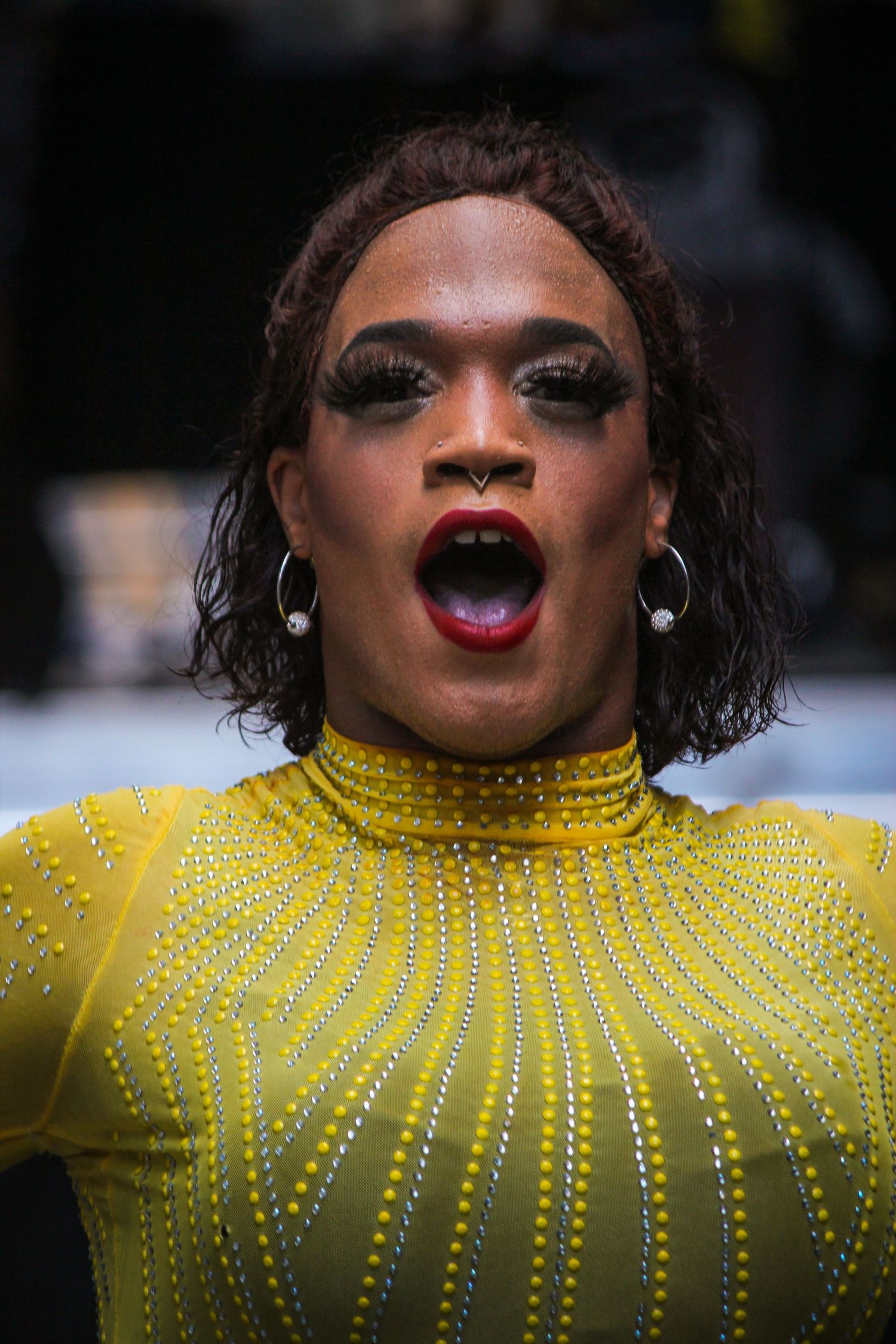 Performer in sparkling yellow high-neck dress singing with dramatic makeup and jewelry.