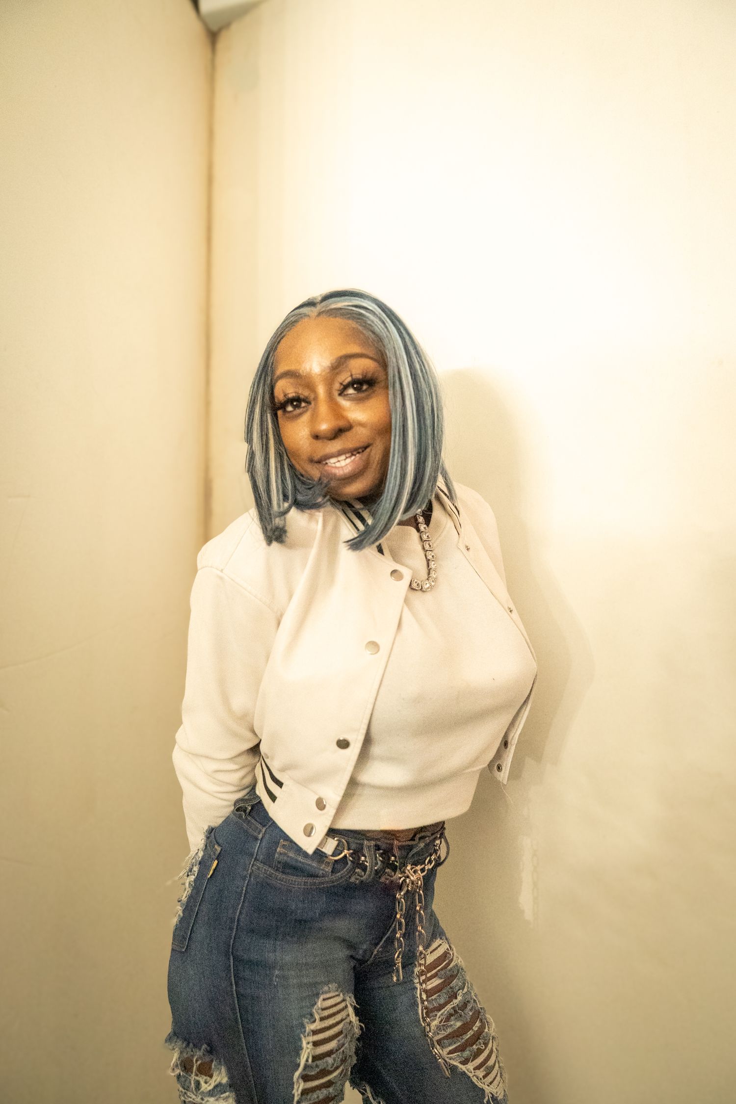 Model in white button-up shirt and distressed jeans poses against beige wall.