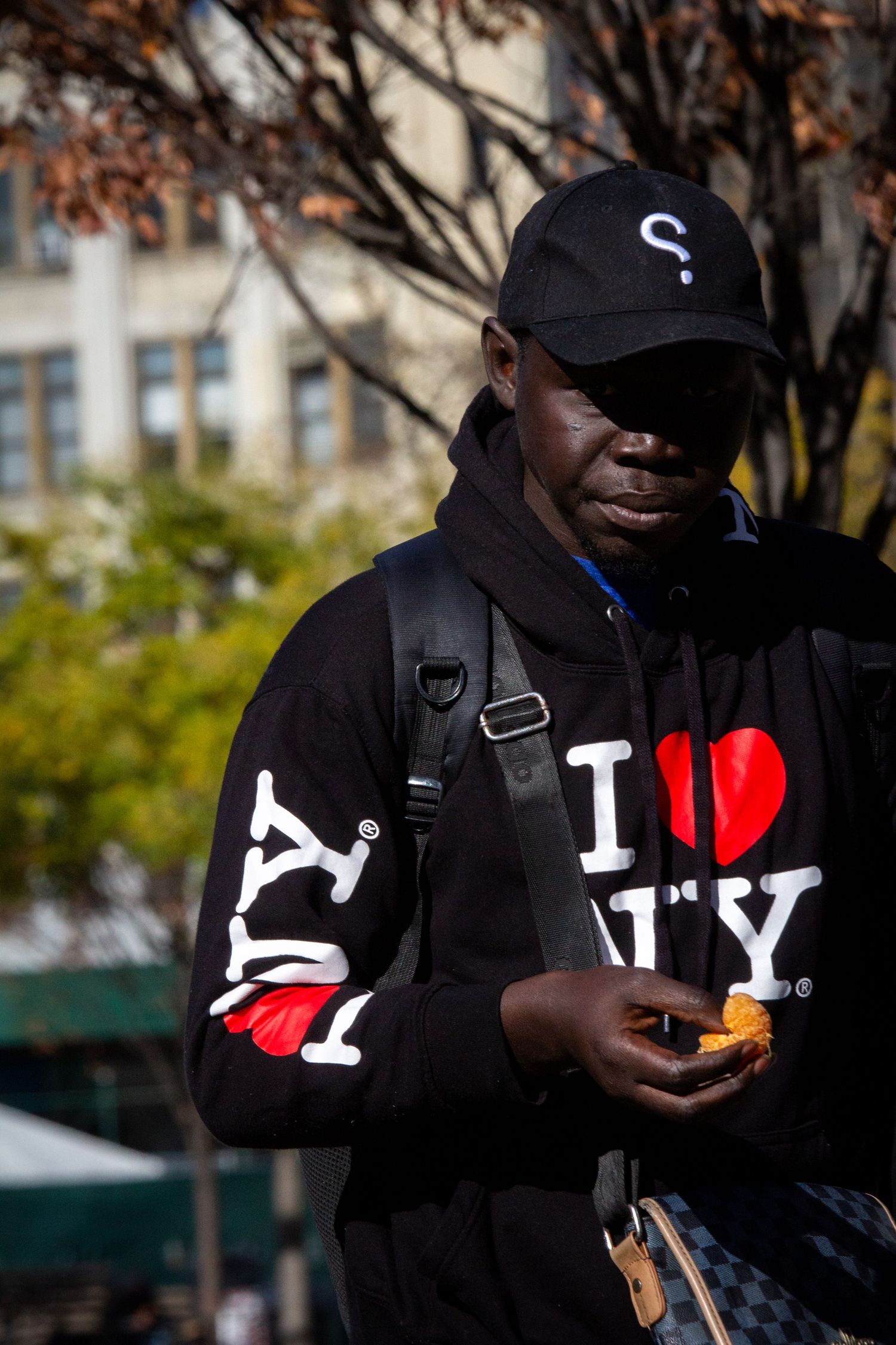 A person wearing an I Love NY hoodie stands near autumn trees.