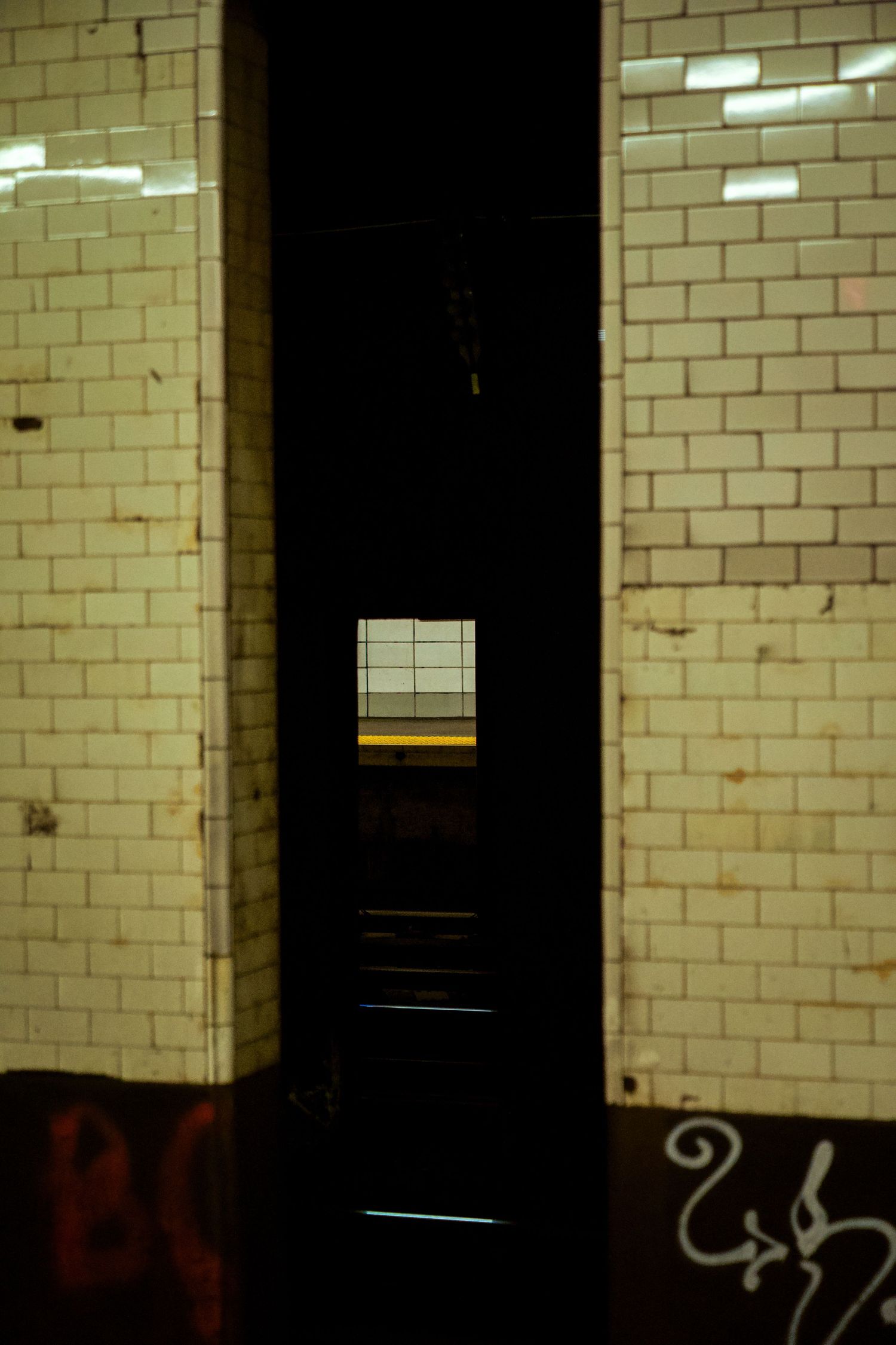 Dimly lit subway tunnel with cream colored brick walls and small window opening.