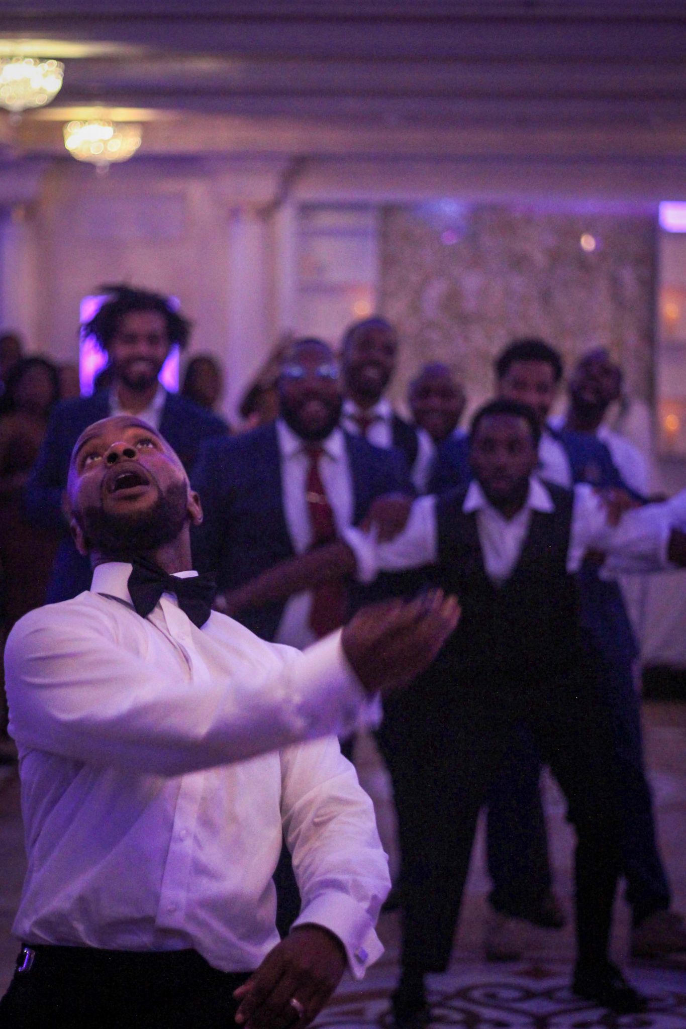 Wedding reception dance floor scene with purple lighting and guests in formal attire.