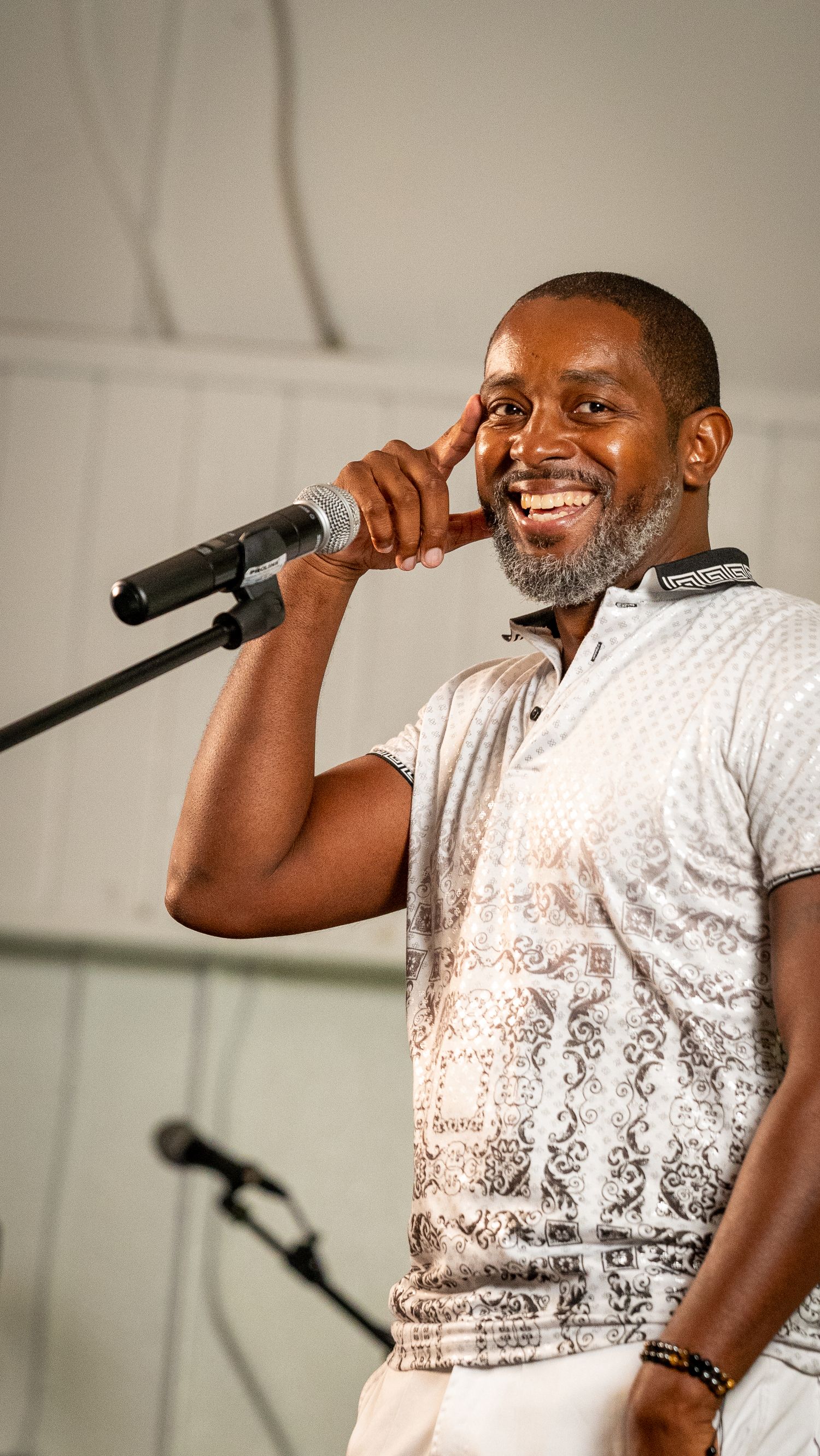 Performer in patterned white shirt sings passionately into microphone on stage.