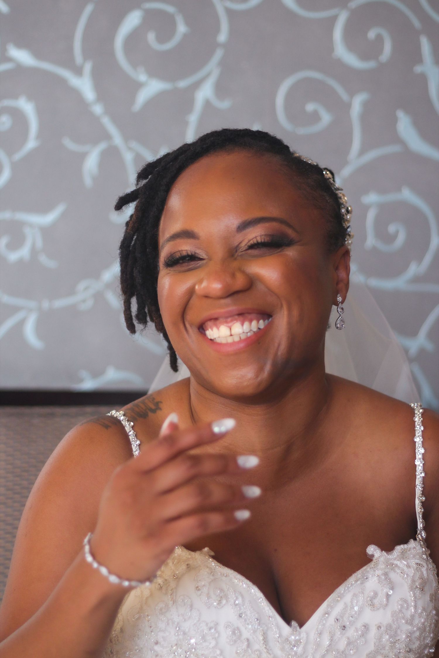 Person in white lace dress smiling with decorative wall pattern backdrop.