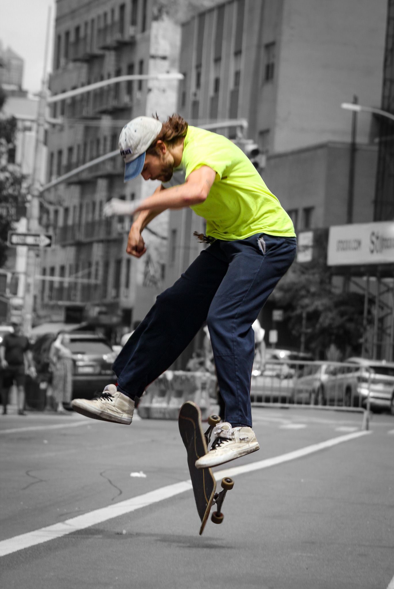 Skateboarder performing an ollie trick on an urban street in selective color with yellow shirt.